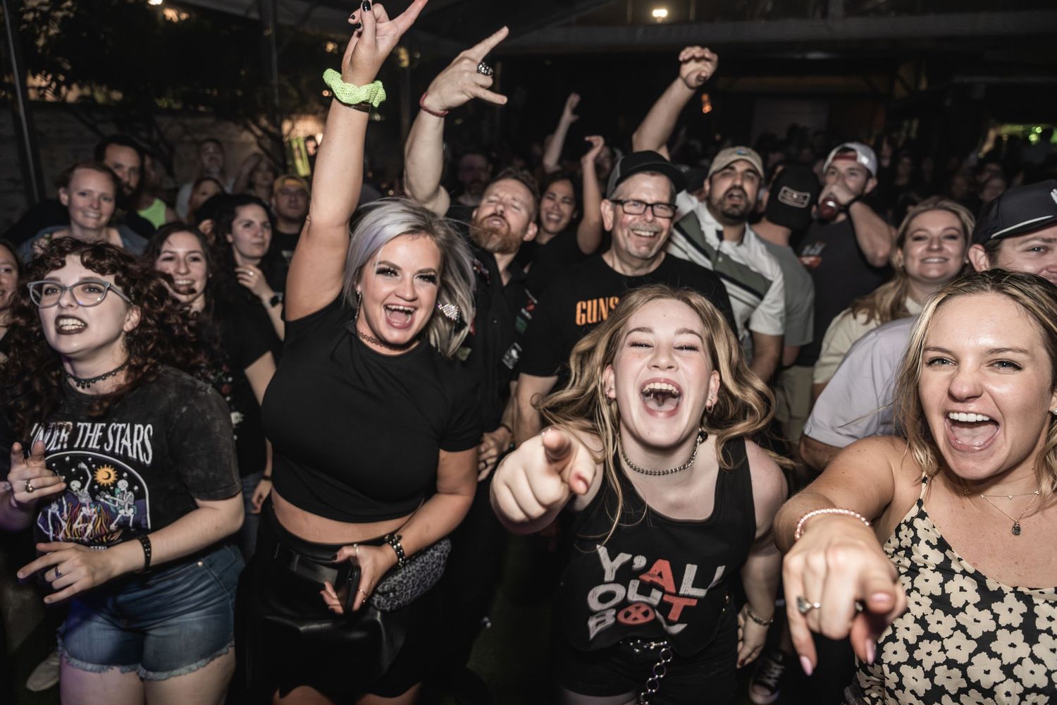 Concert-goers cheer enthusiastically with raised arms during a live music performance.