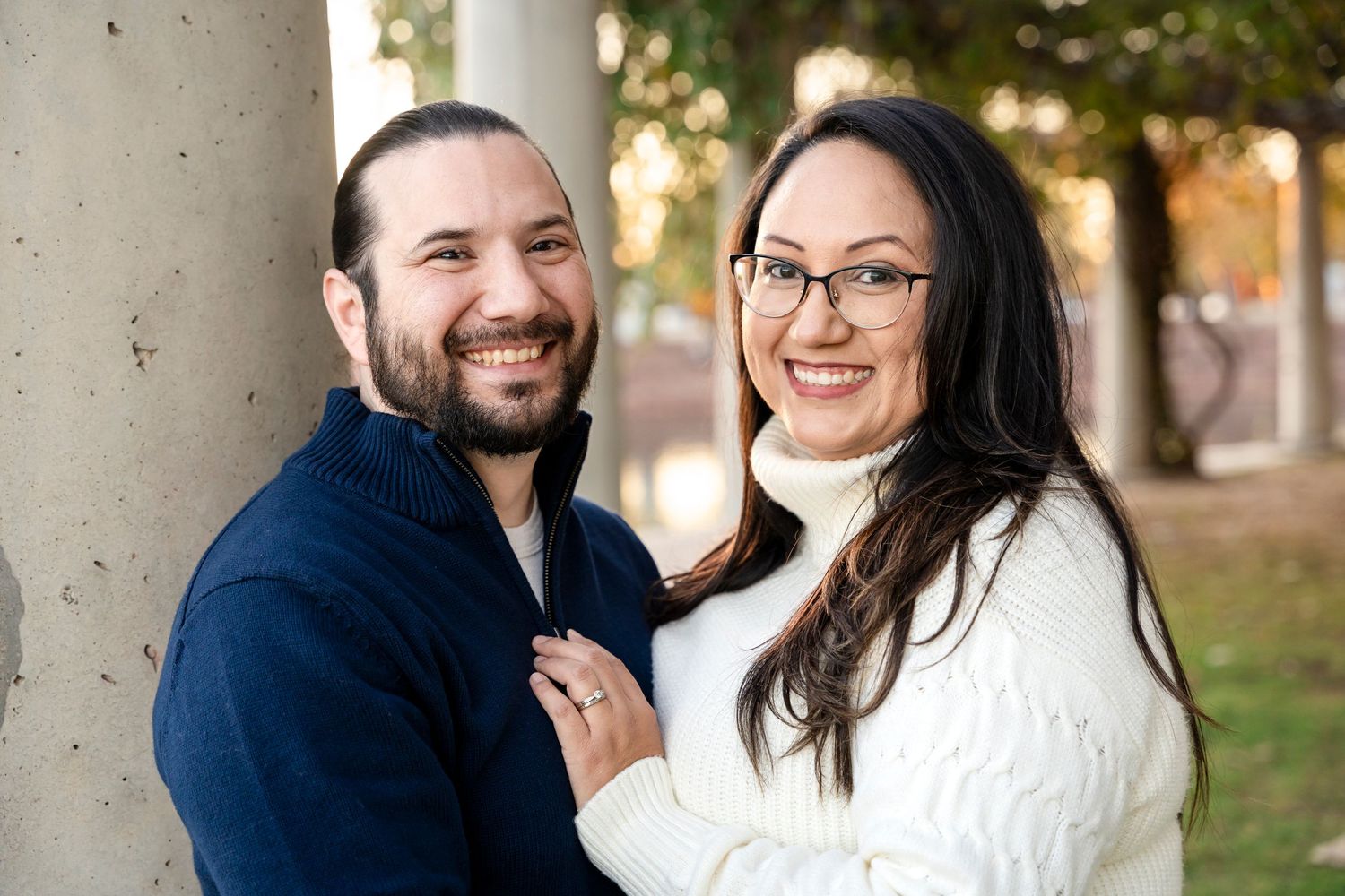 Couple in navy and white sweaters embrace while smiling outdoors.