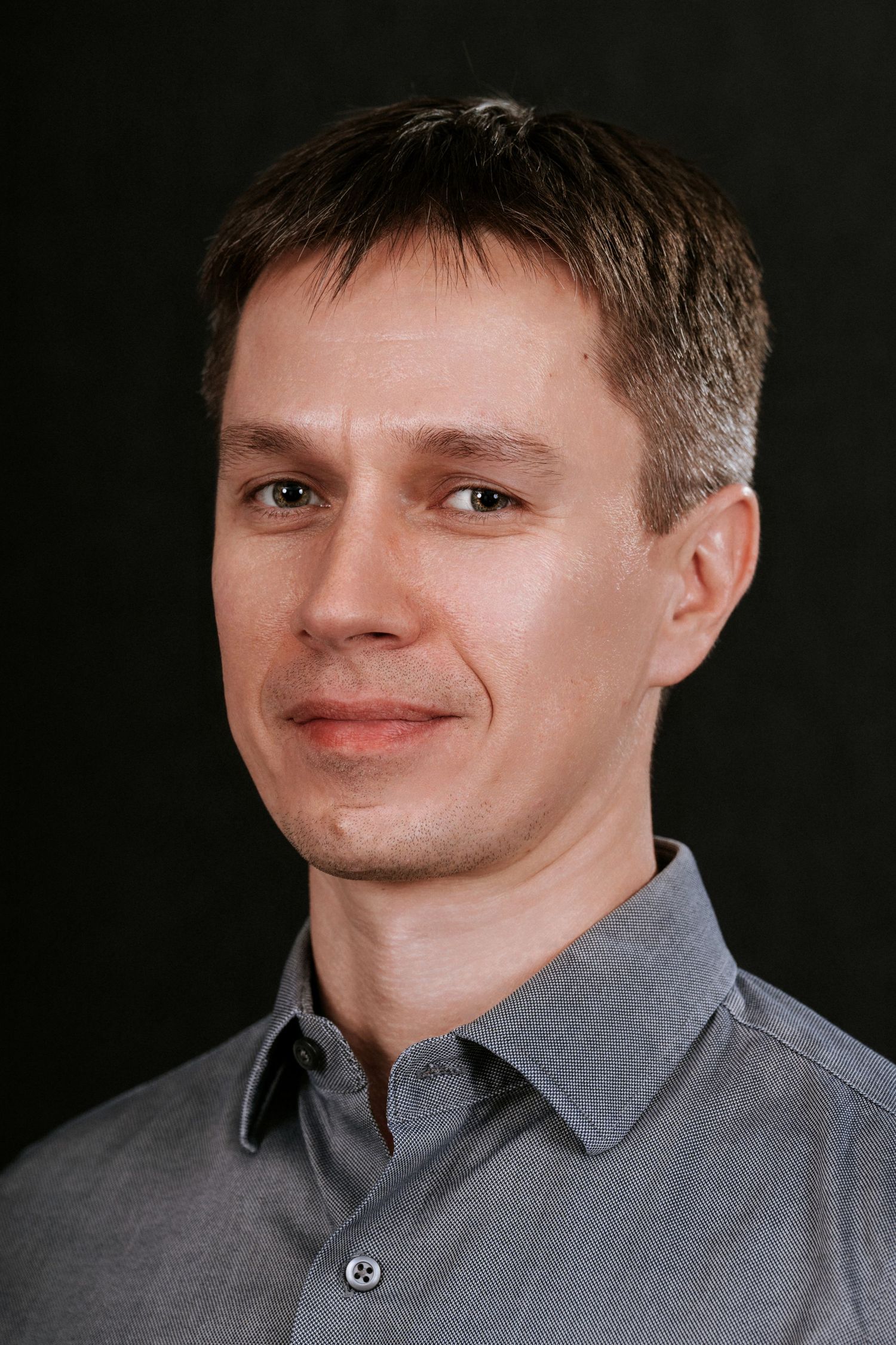 Professional portrait against black backdrop showing person in grey business casual attire.
