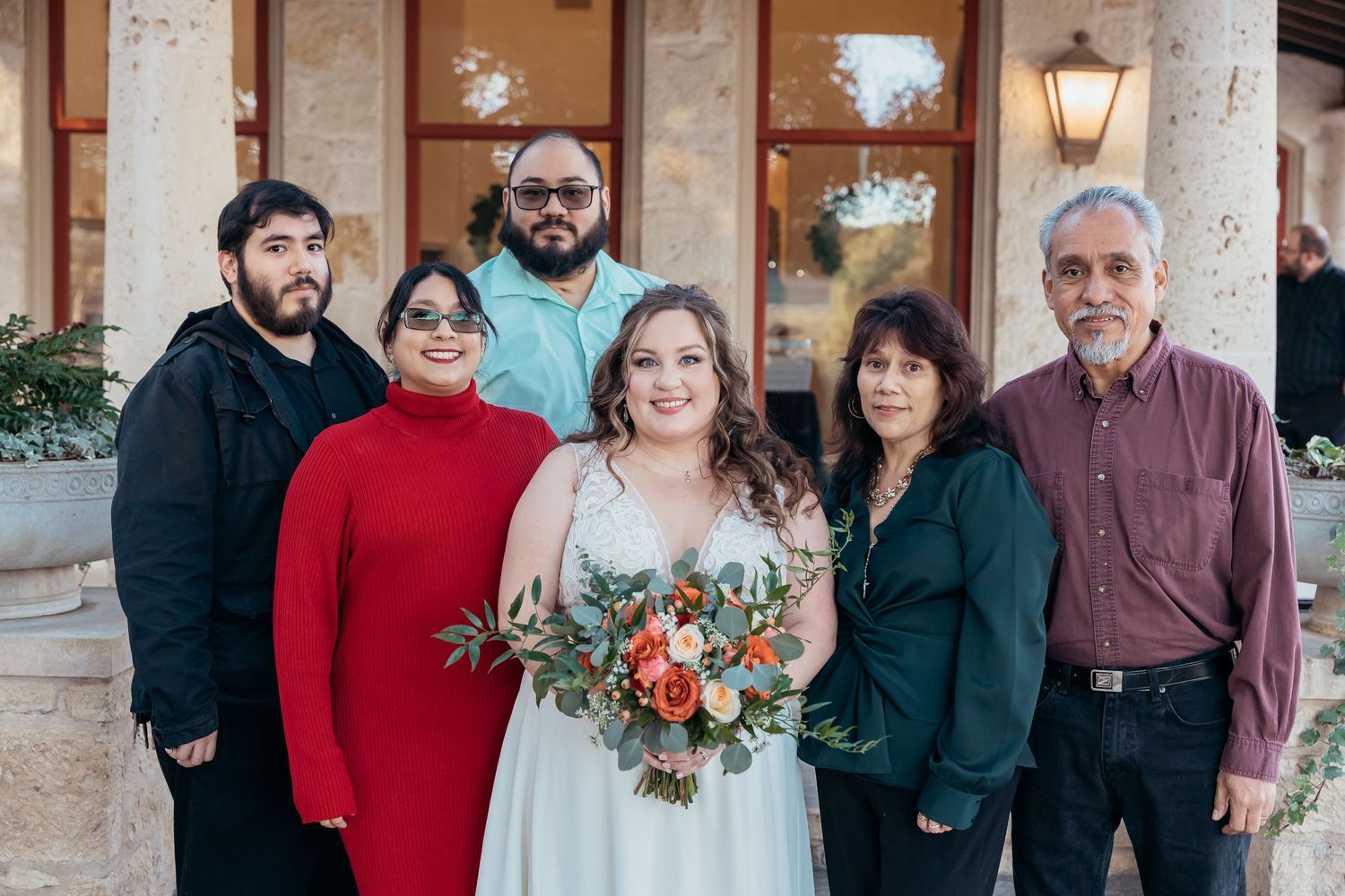 Small family group poses for formal wedding portrait against stone building.