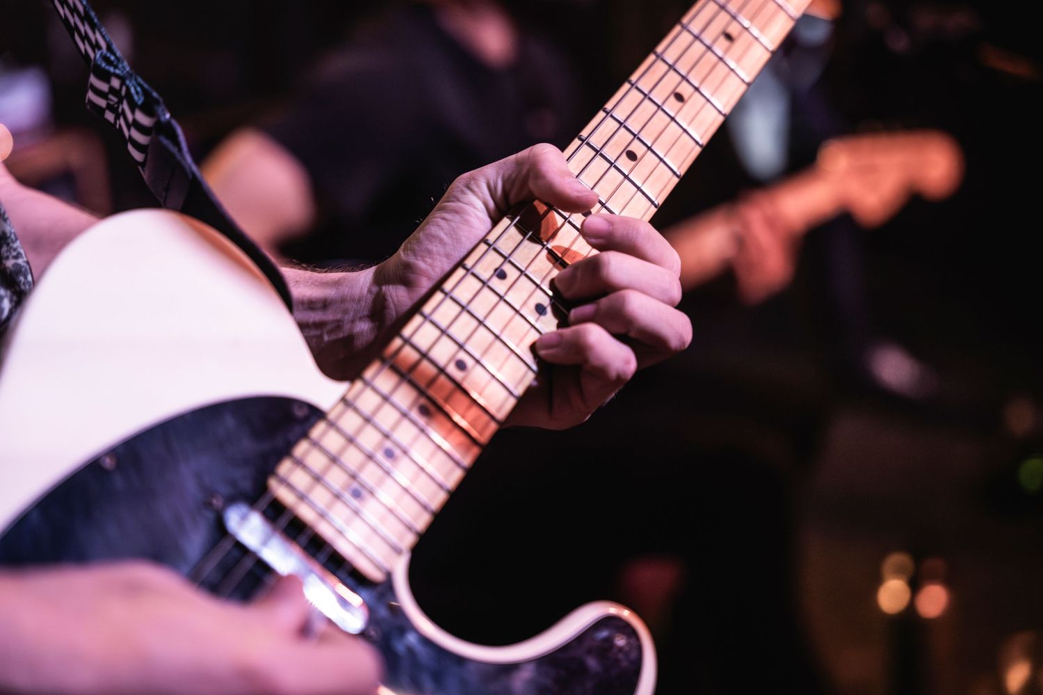 Close-up shot of hands playing electric guitar with maple neck during live performance.