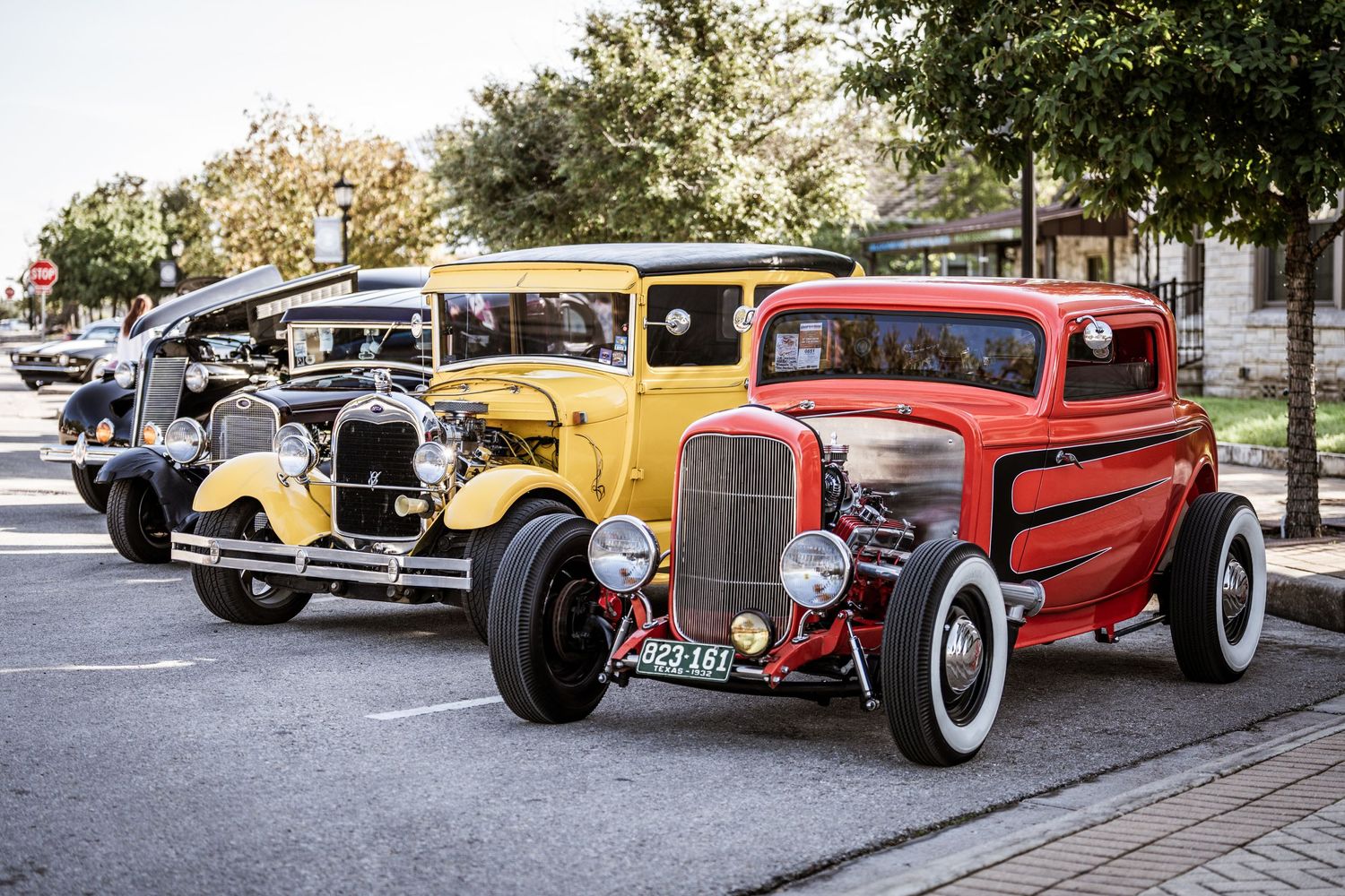 Row of vintage hot rods including a yellow and red custom classic cars at an outdoor show.