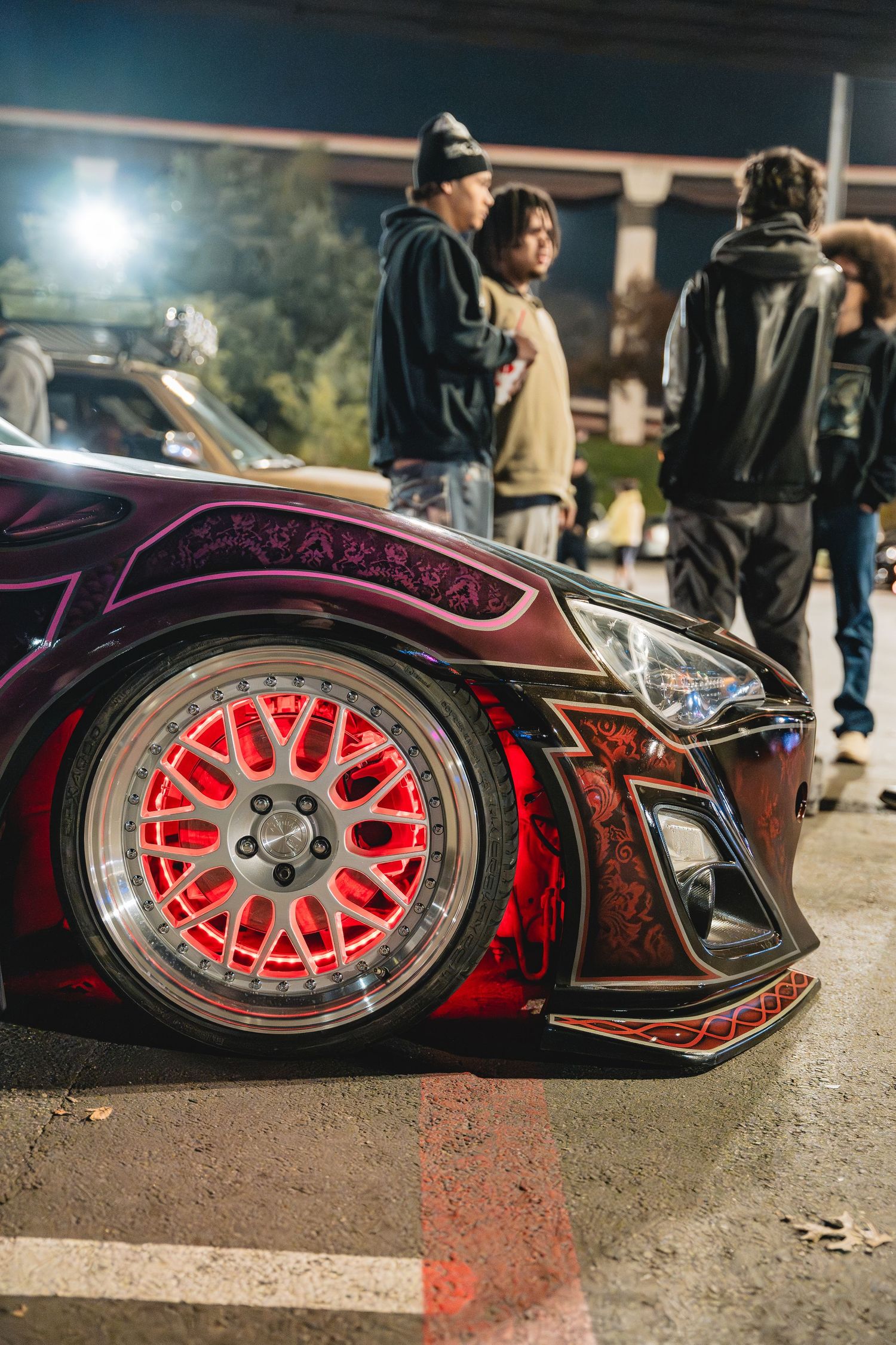 Close-up of bright red custom wheels on a modified sports car at a nighttime car meet.