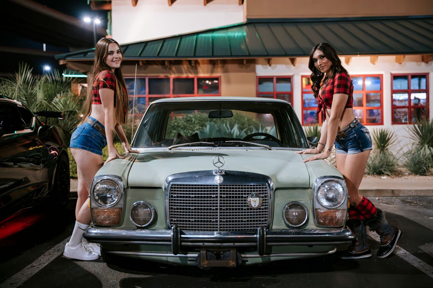 Classic Mercedes-Benz sedan with plaid-dressed models posing at night outside a restaurant.