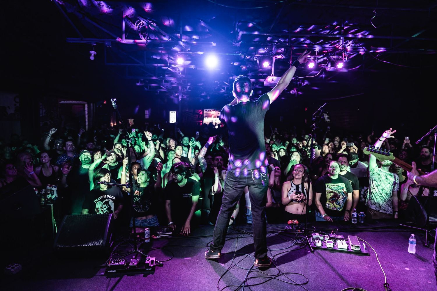 Energetic concert crowd illuminated by blue and green lights beneath a disco-lit ceiling.