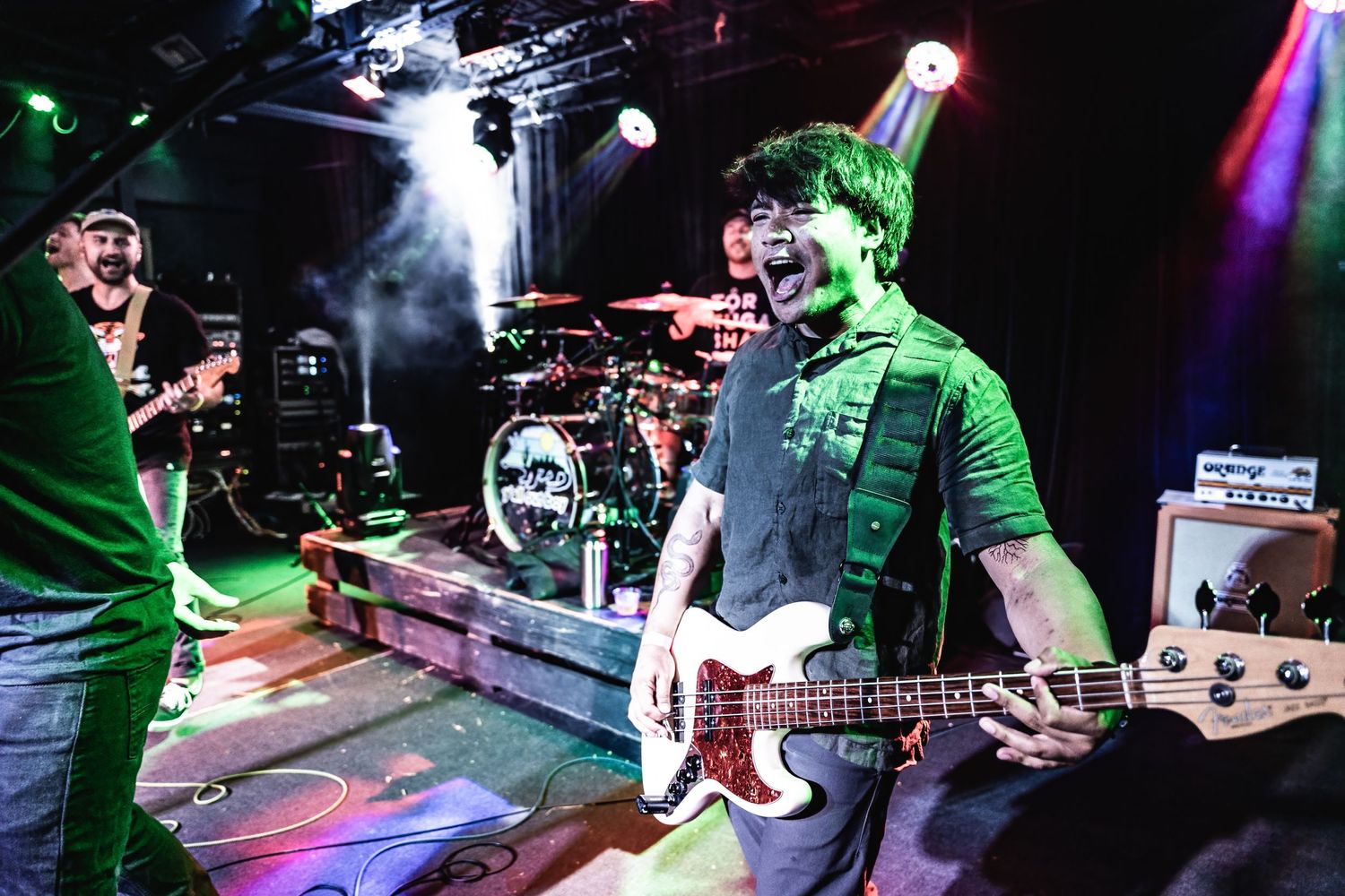 Band members perform energetically under green stage lighting with smoke effects.