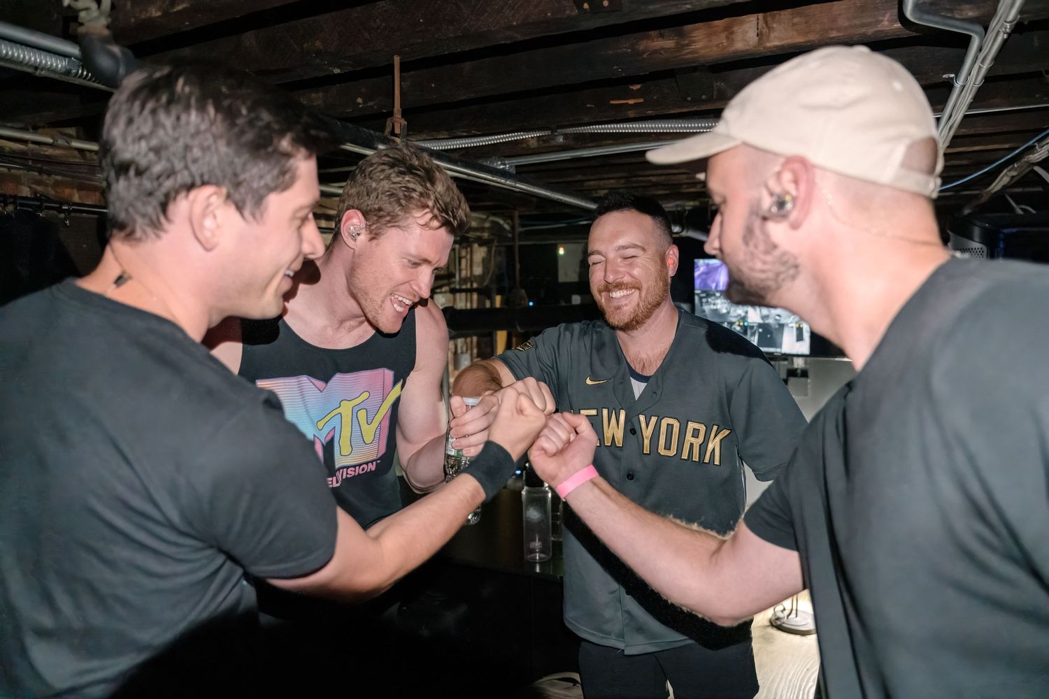 Musicians share an energetic handshake moment in a dimly lit venue setting.