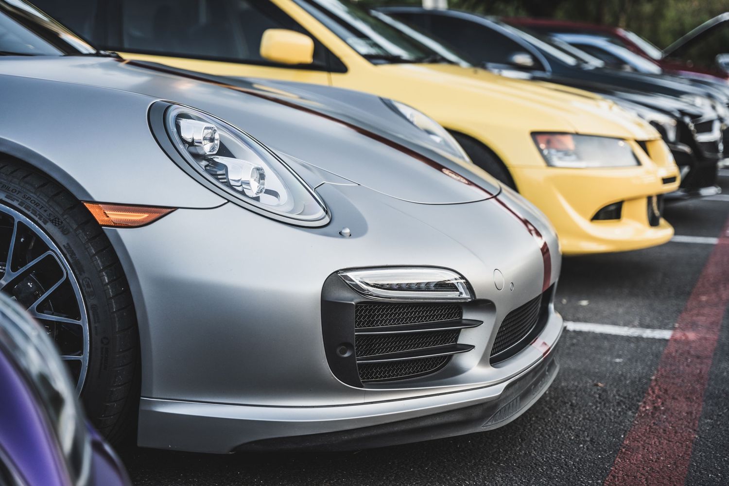Close-up view of a silver Porsche 911 front end with a yellow sports car in the background.