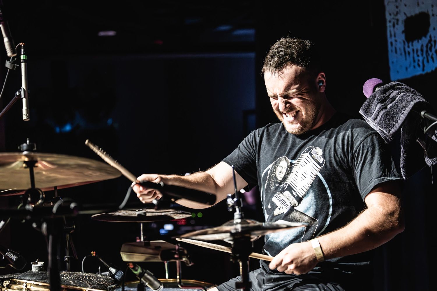 Passionate drummer performs with drumsticks in motion on dimly lit stage.