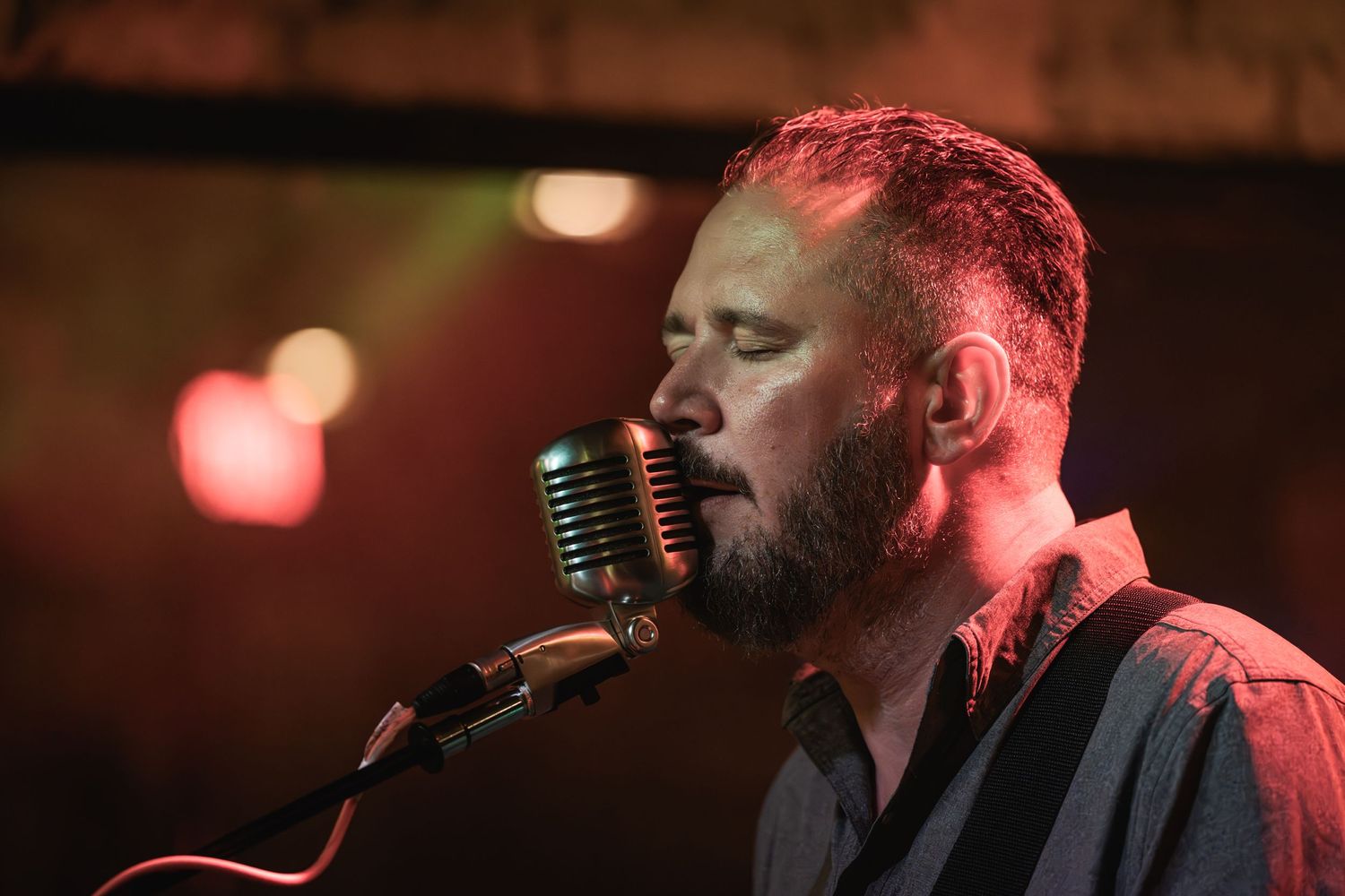 Musician singing into vintage microphone under dramatic red lighting.