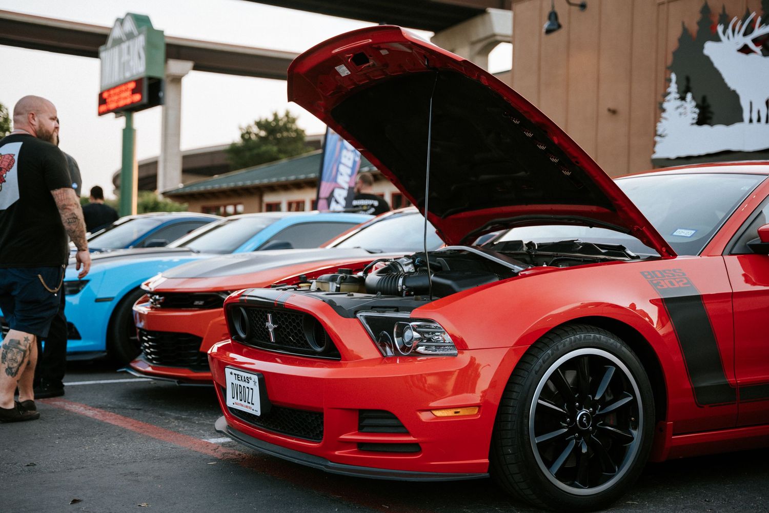 Red Ford Mustang with hood open on display at outdoor car meet.