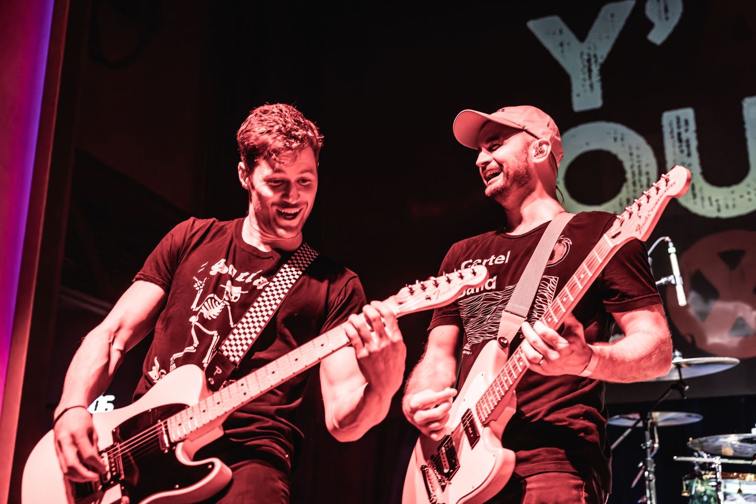 Two guitarists performing together on stage with matching black attire.