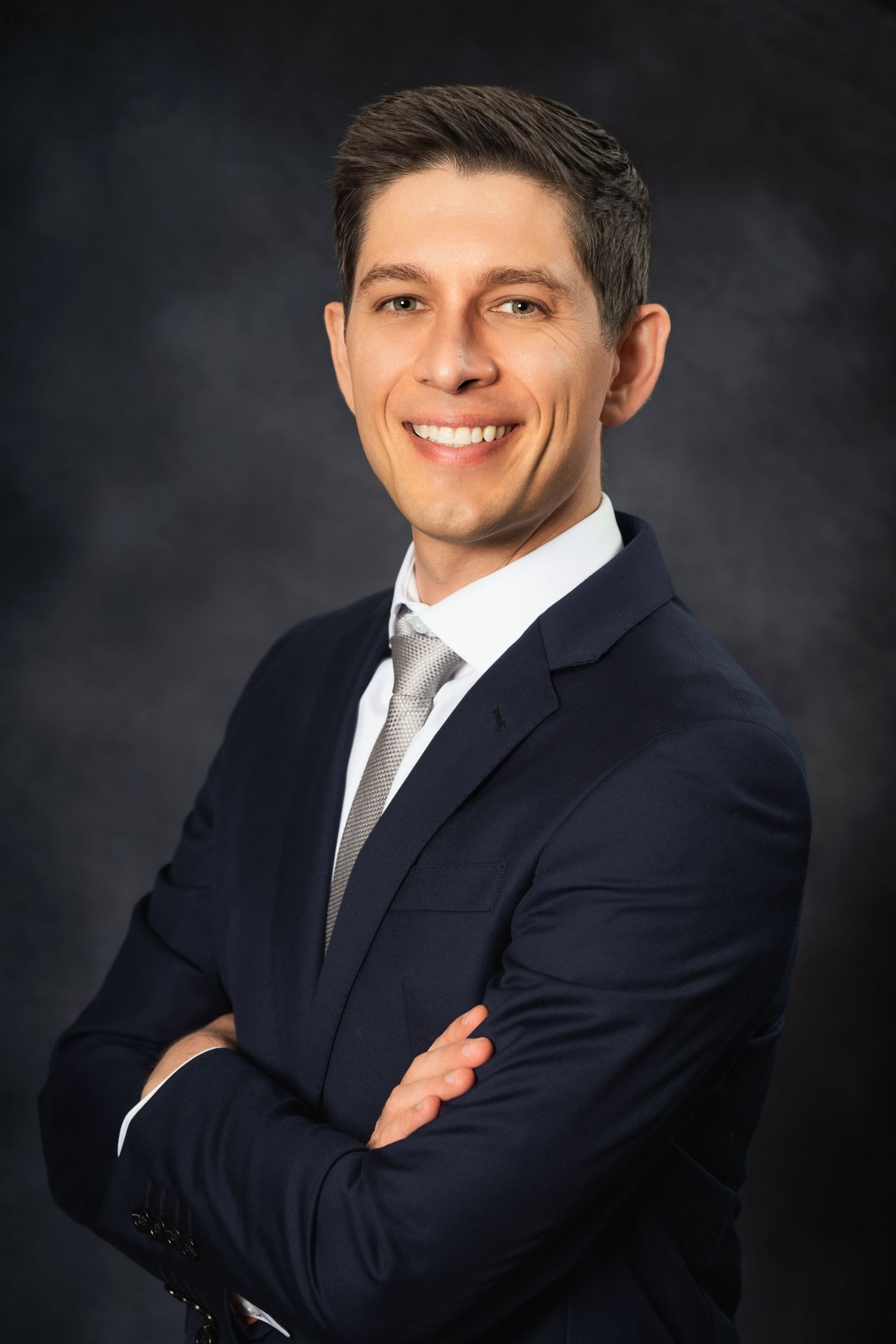 Business portrait of a professional in a dark suit with arms crossed and confident smile.
