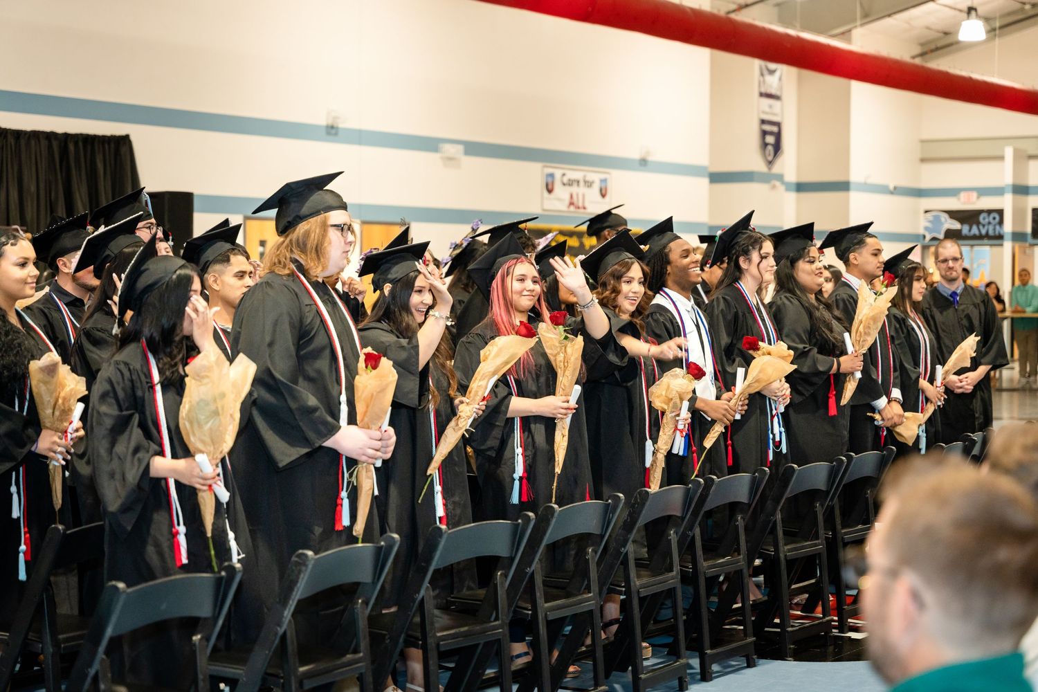 Graduates stand in rows wearing black caps and gowns during commencement ceremony.