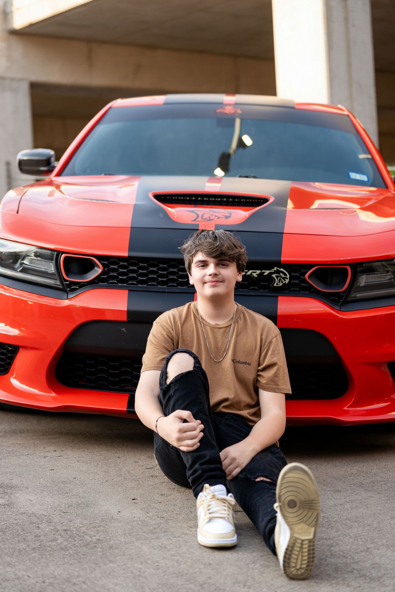 A portrait in front of a red Dodge Charger with black racing stripes and performance modifications.