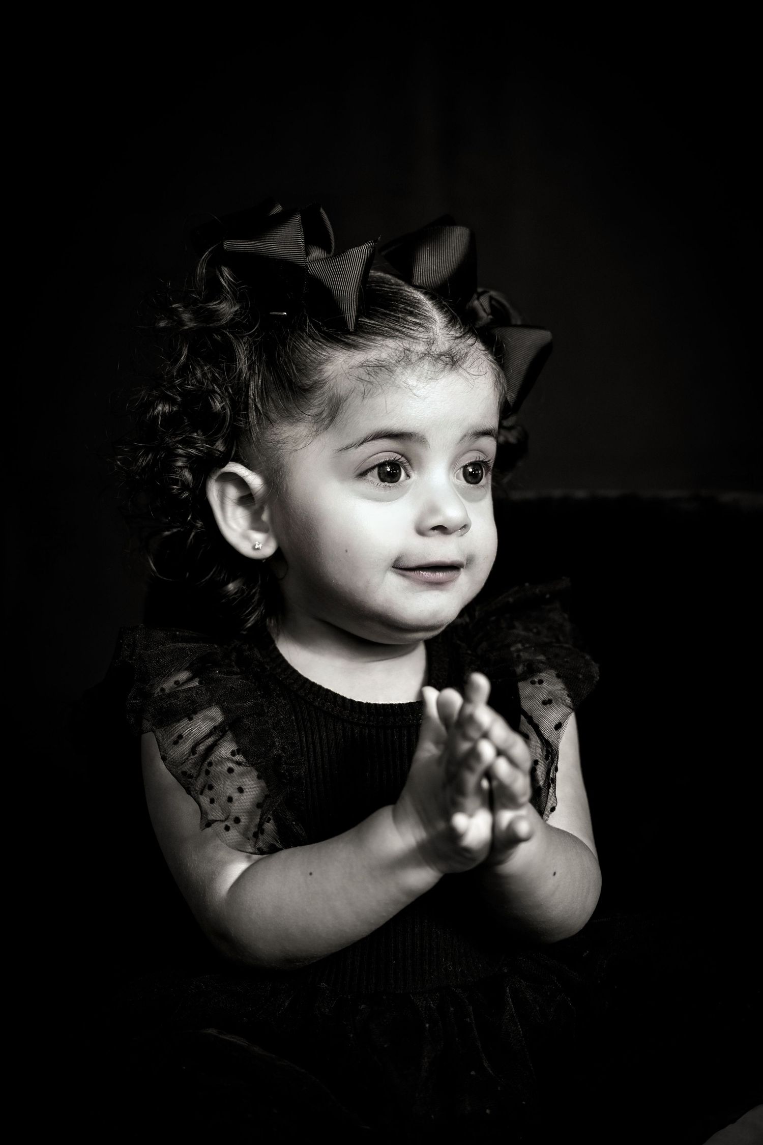 Black and white portrait of smiling toddler with hair bows clapping hands.