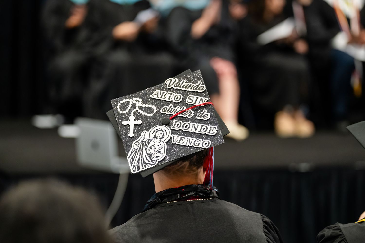 Decorated graduation cap with Spanish text and cross design at a commencement ceremony.