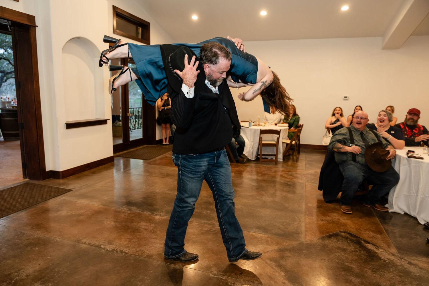 Man lifting woman during lively dance performance at indoor wedding reception event.
