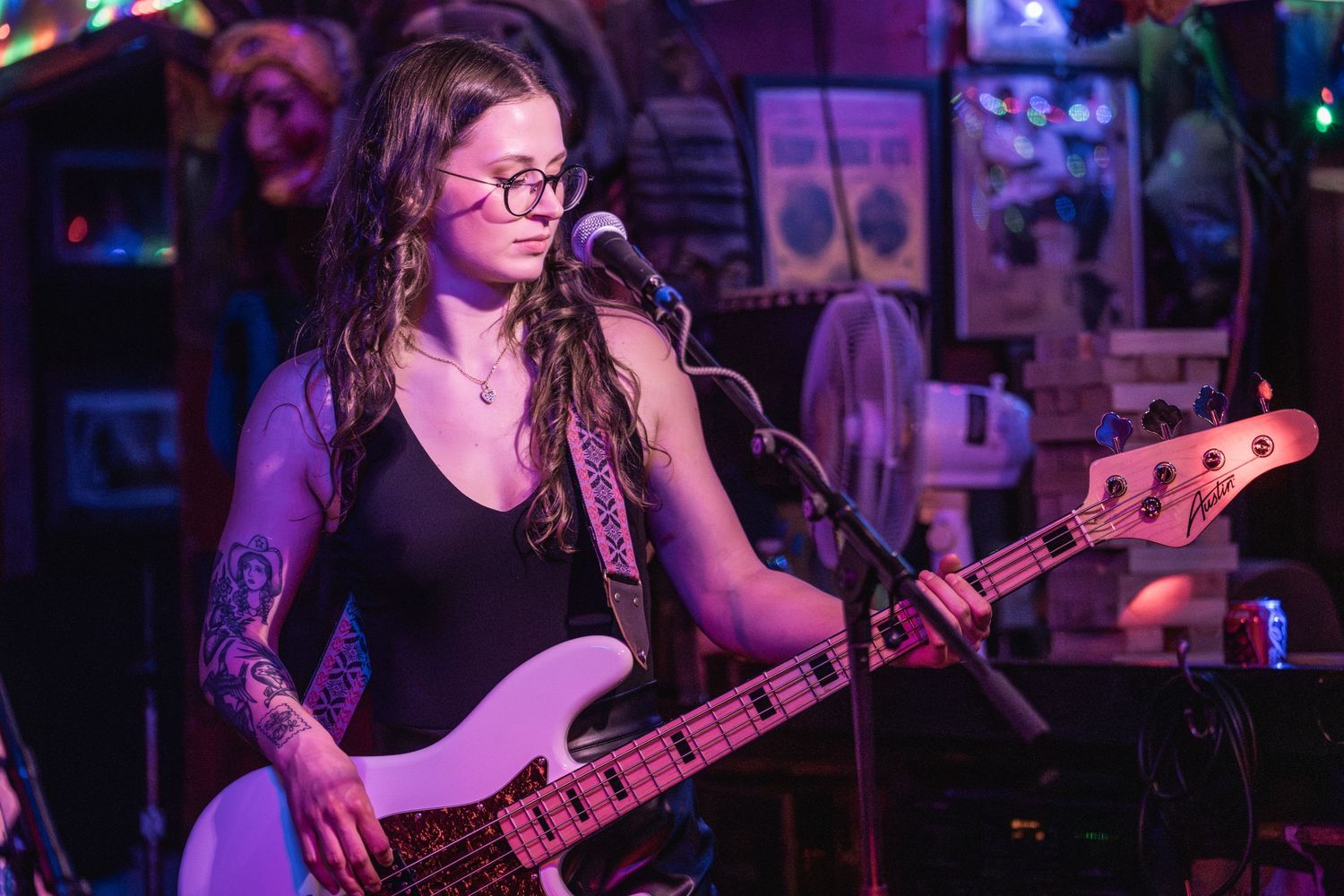 A bass guitarist performs on stage in purple lighting at a live music venue.