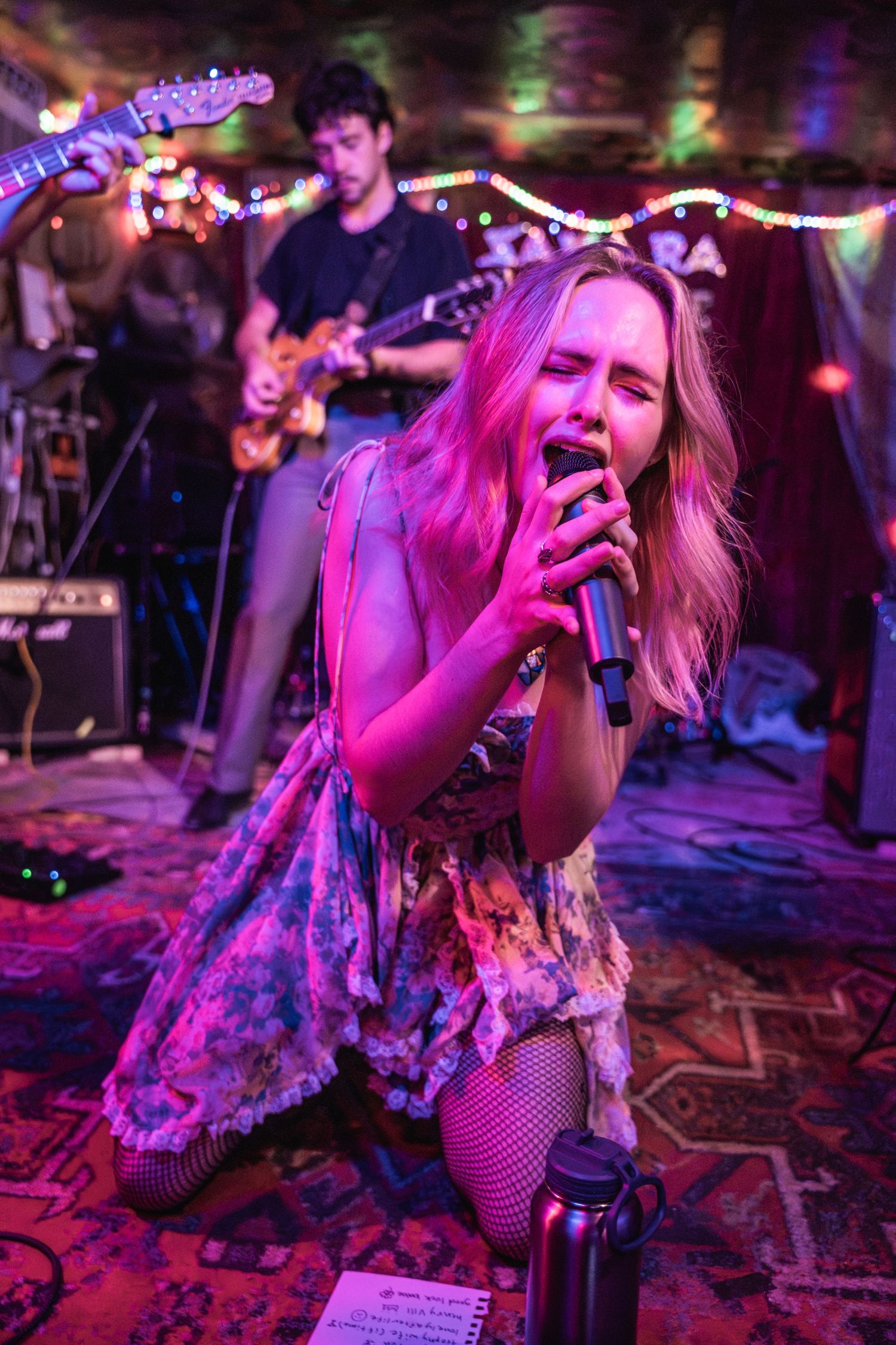 Singer performs passionately on stage under vibrant purple lighting with band in background.