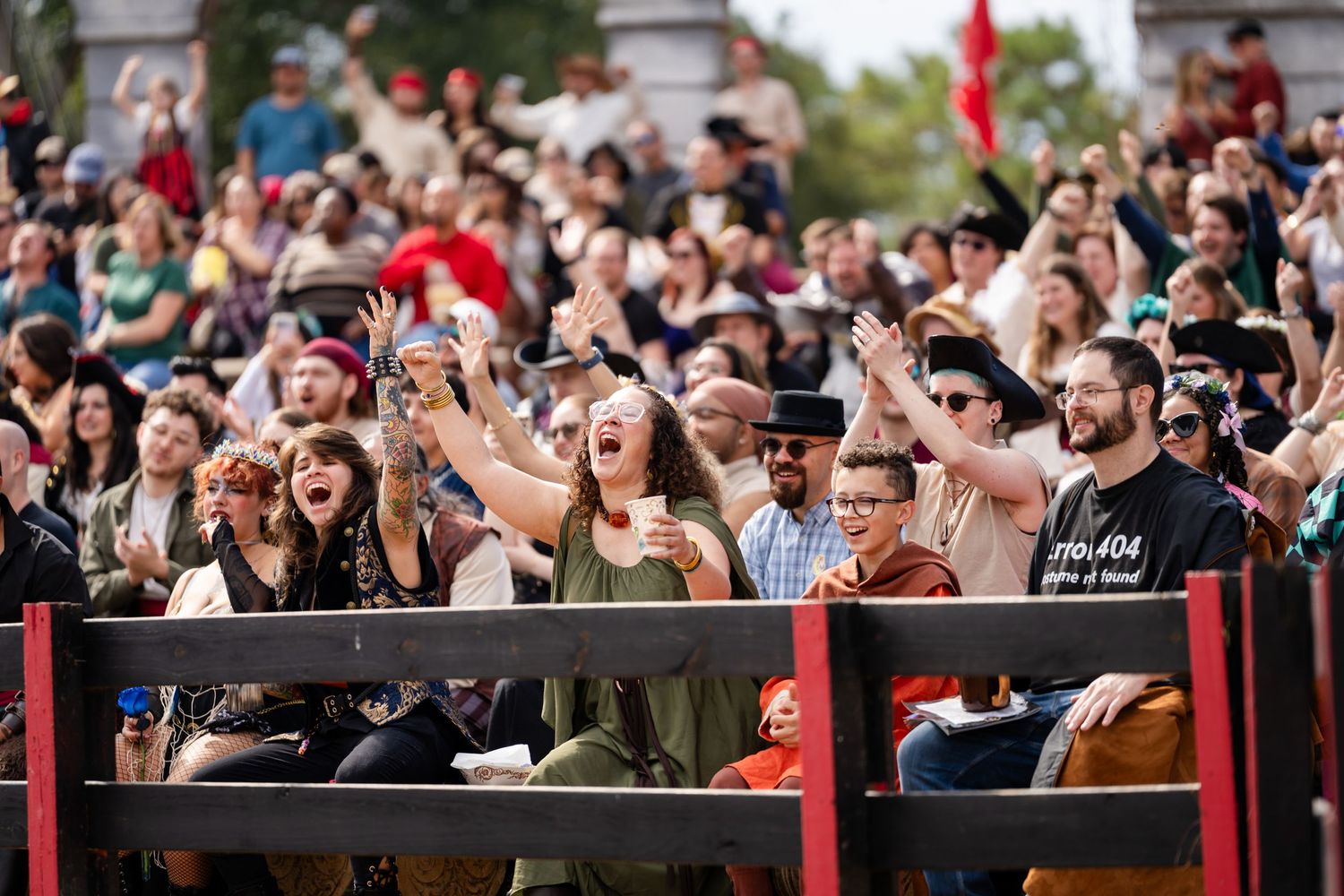 Excited crowd of festival attendees cheer and take photos from behind metal barriers at an outdoor event.