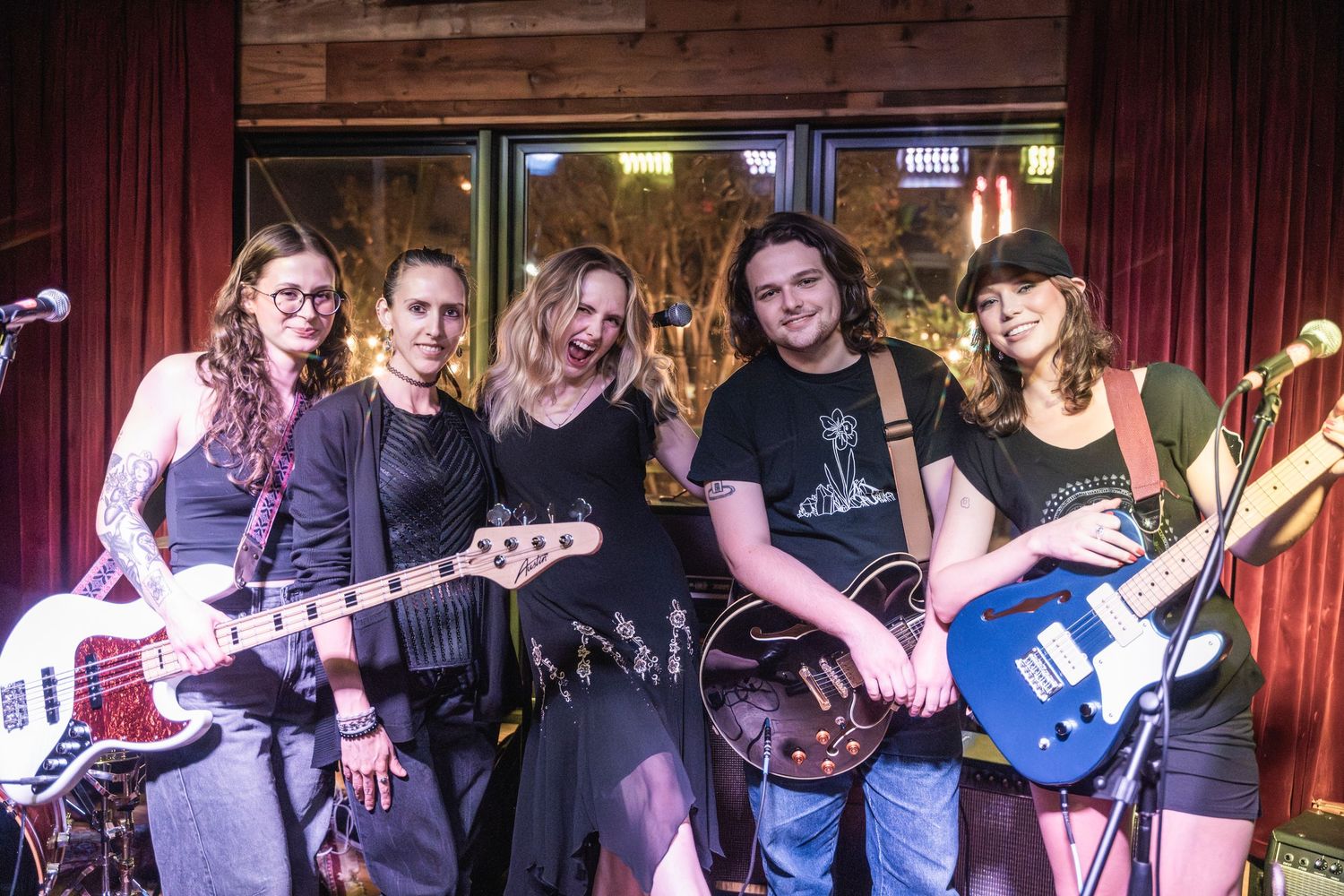 A group of musicians performing on stage with guitars and instruments in a dimly lit venue setting.