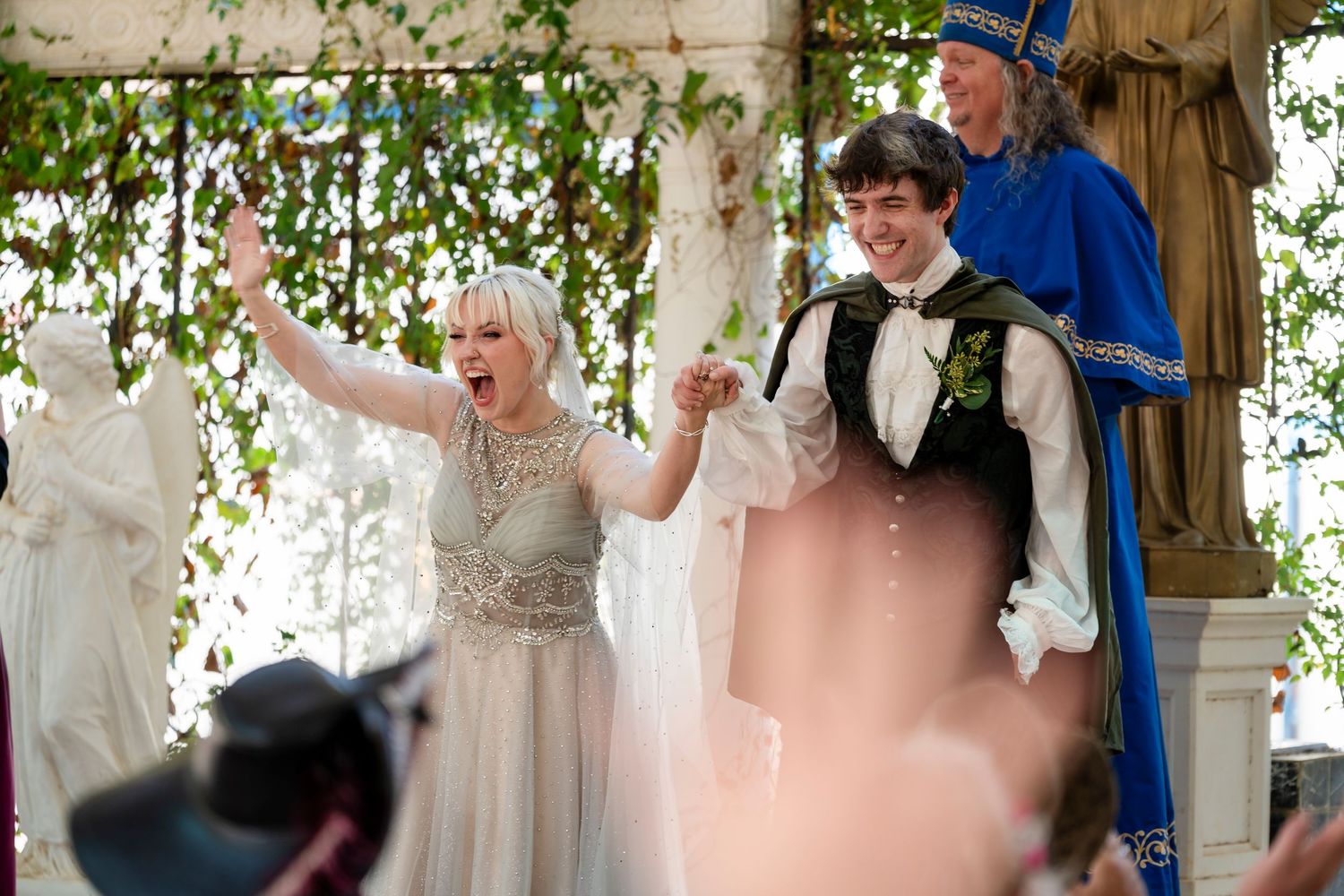 Wedding guests dance and celebrate together under a white tent decorated with hanging greenery and fabric draping.