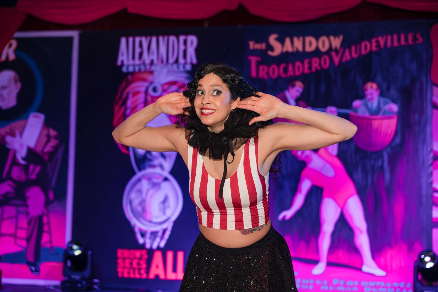 Performers dance on stage in red and white striped costumes under vibrant purple lighting during a theatrical show.