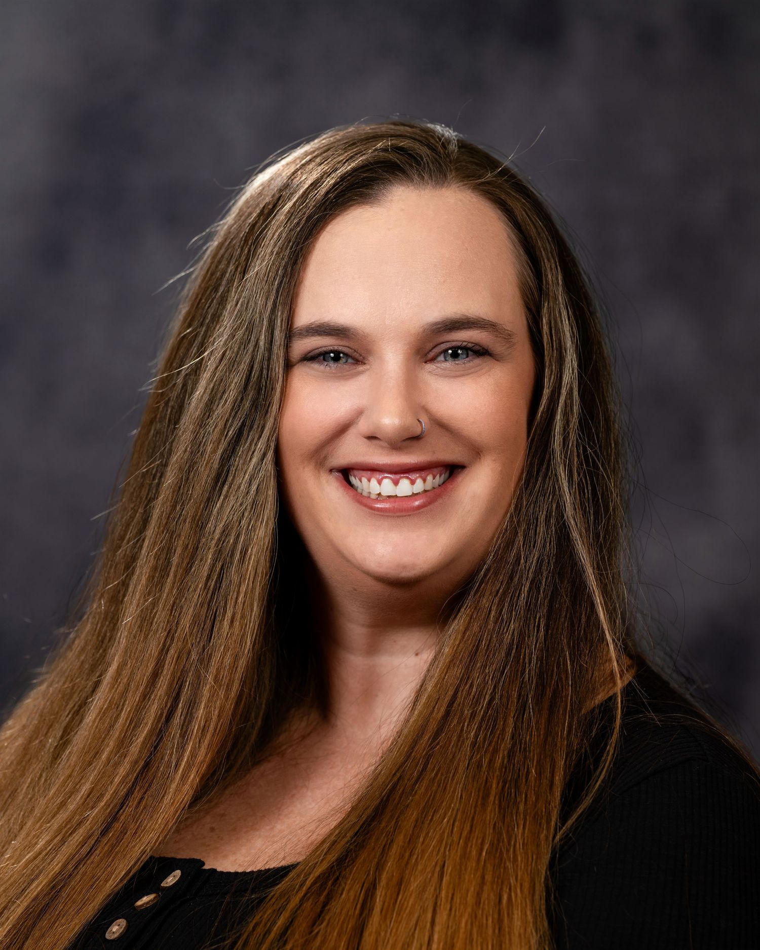 Professional headshot portrait of someone with long brown hair wearing a black top against a dark background.