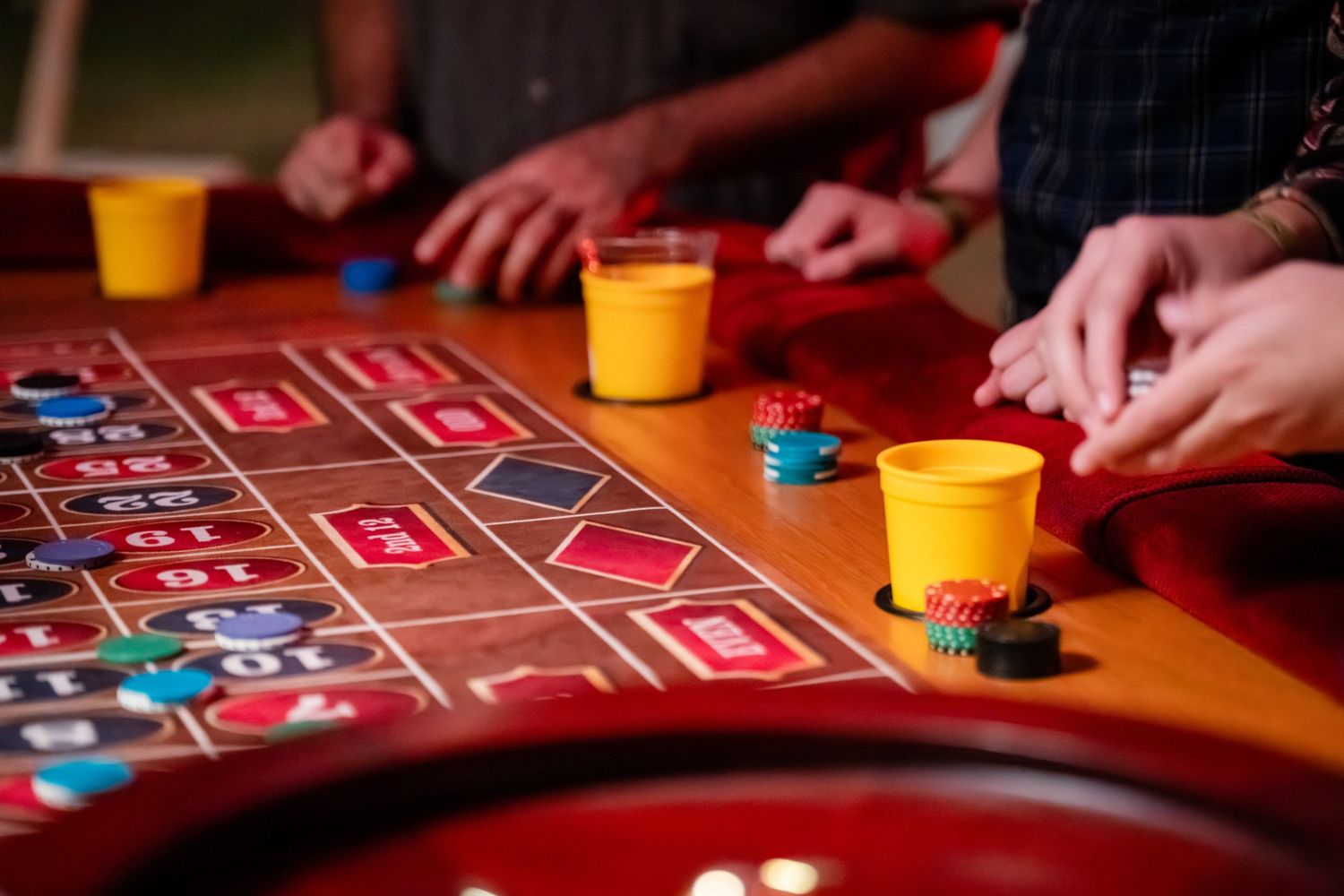Close-up view of hands placing bets with blue chips on a red casino craps table with yellow cups.