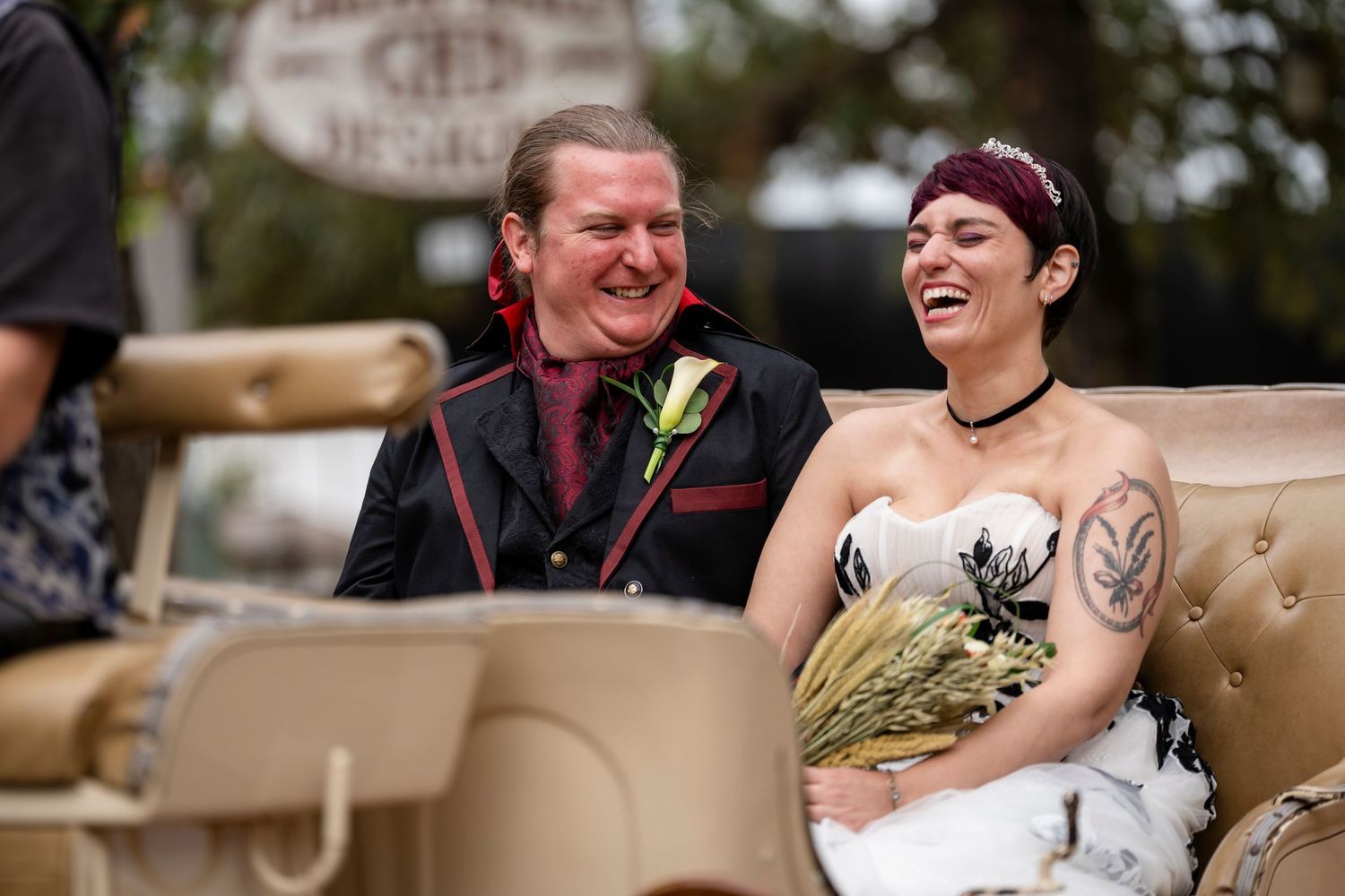 A couple laughs together while sitting on a beige couch during a wedding celebration.