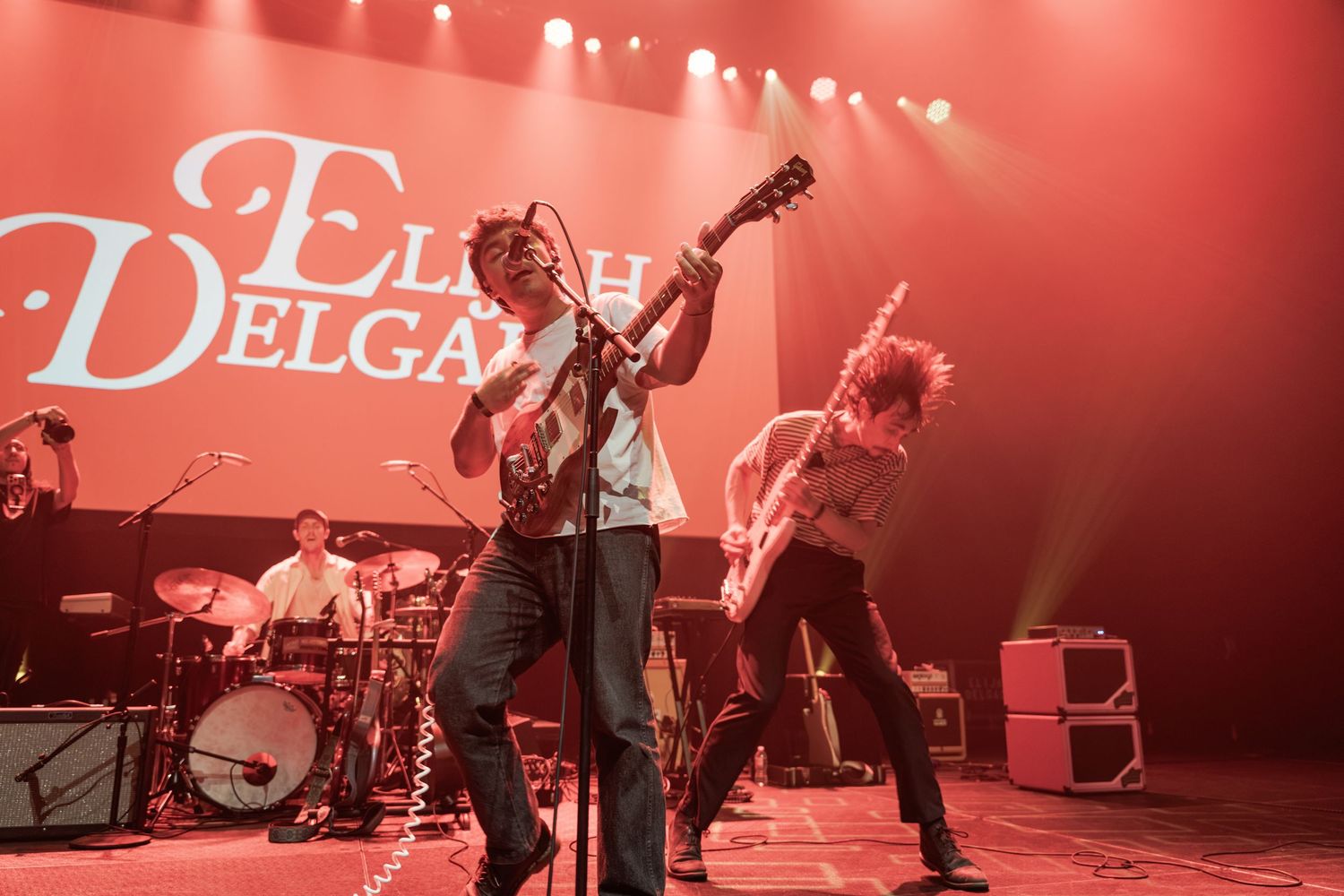 Elijah Delgado band performing live on stage with guitars and drums under red and white stage lights.