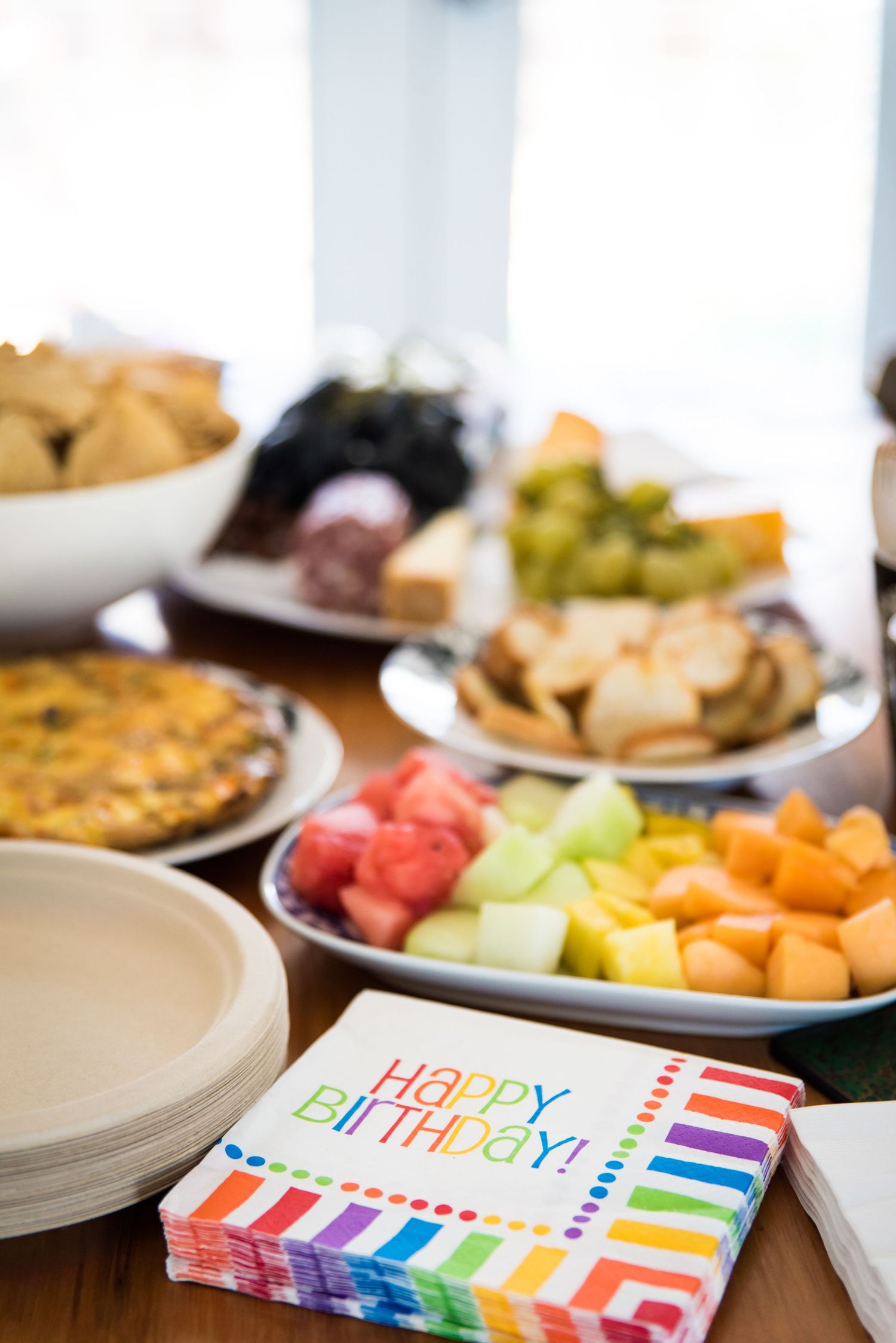 Colorful birthday party table setting with rainbow napkins, plates of fresh fruit, and festive decorations.