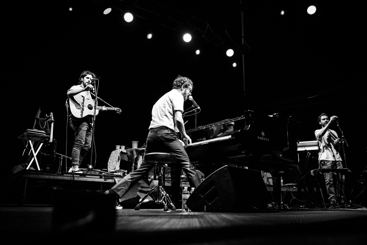 Musicians perform on stage during a live concert with dramatic black and white lighting effects.