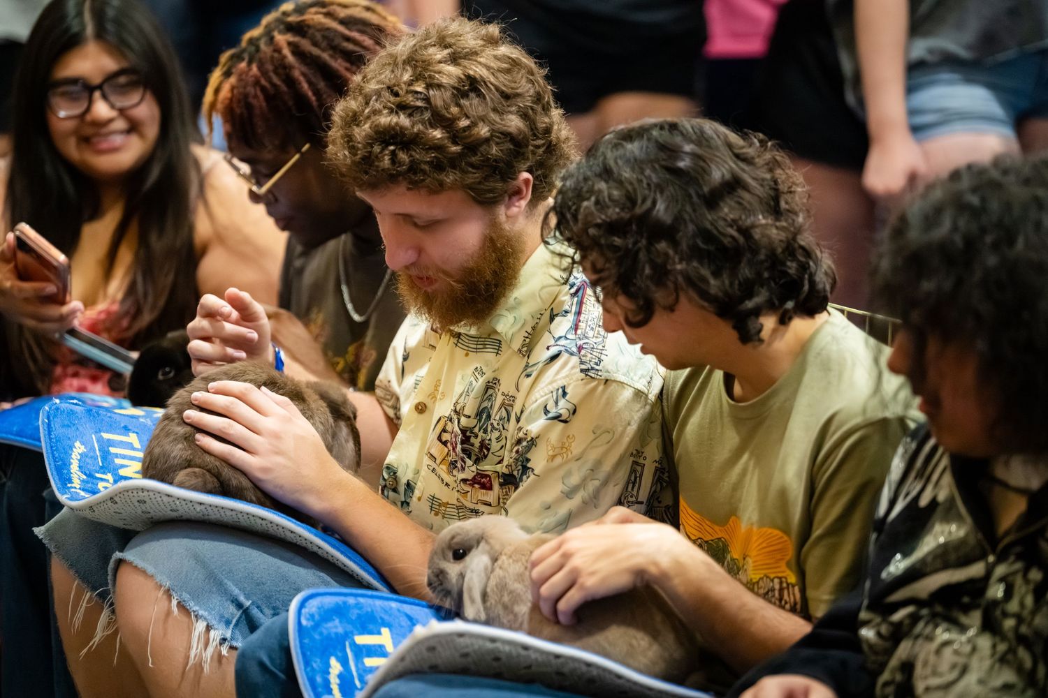 Group of young adults sitting together at an indoor event, looking down at something in a casual social setting.