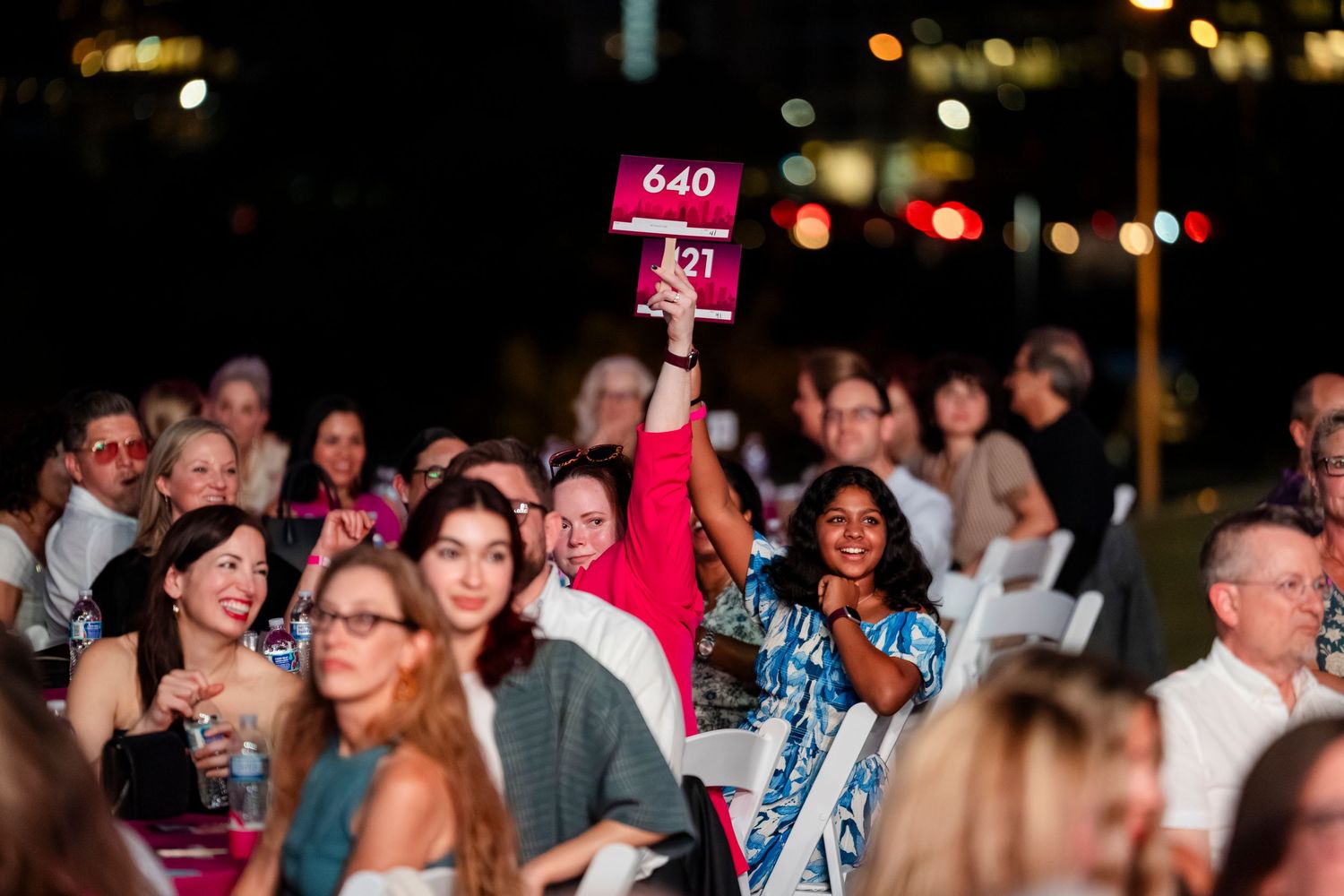 Crowd of people enjoying a nighttime event with colorful lighting and festive atmosphere.