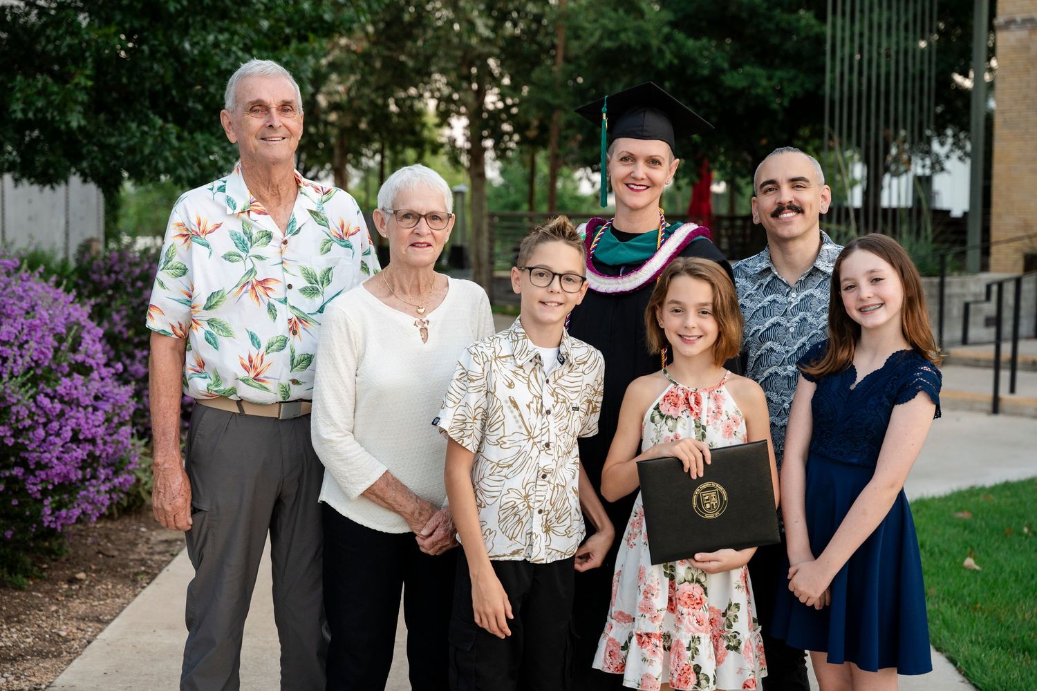 A group of people stand together in a garden setting wearing casual summer attire.