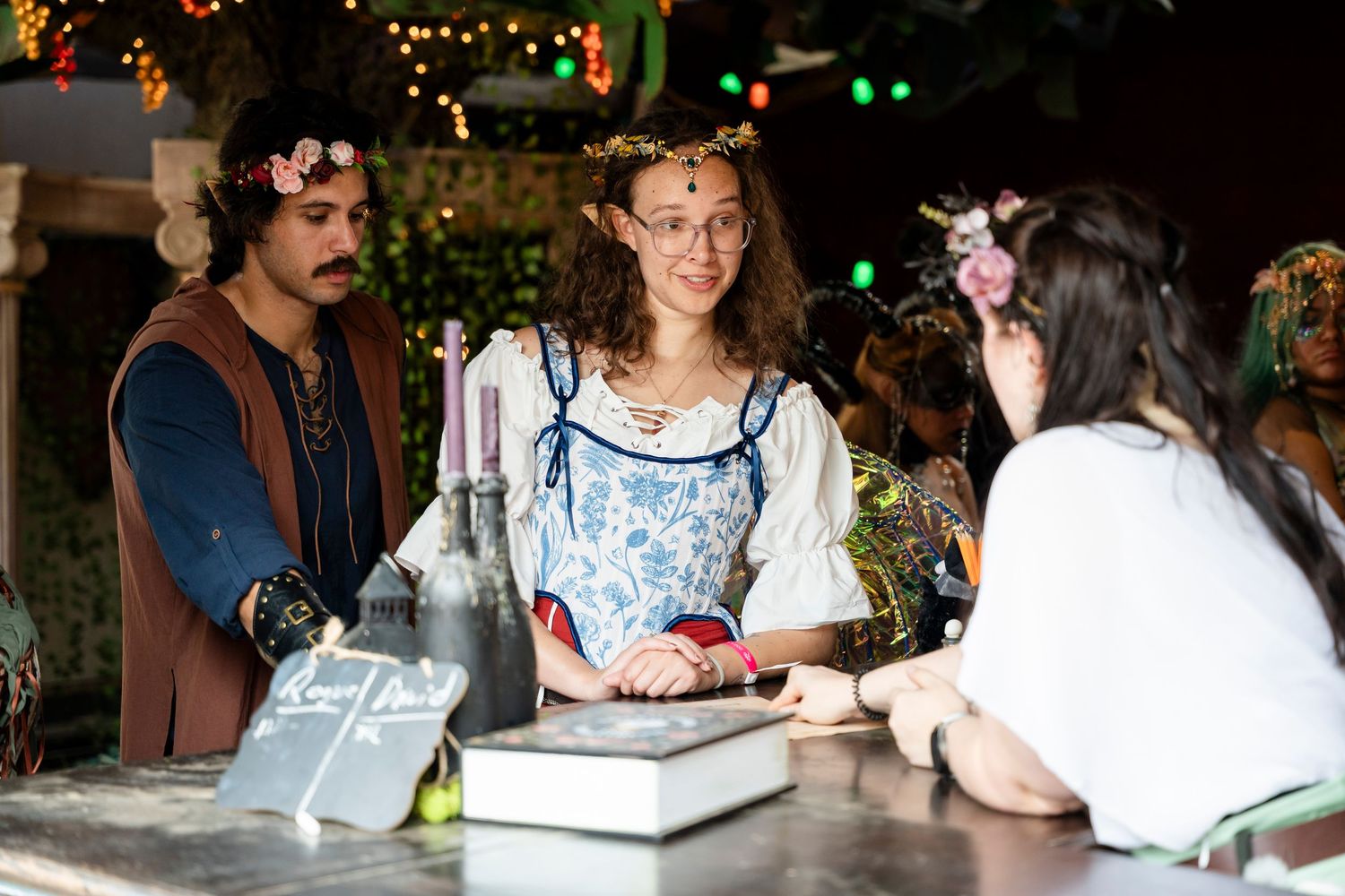 People gathered around tables at an outdoor evening event with string lights creating a warm, festive atmosphere.