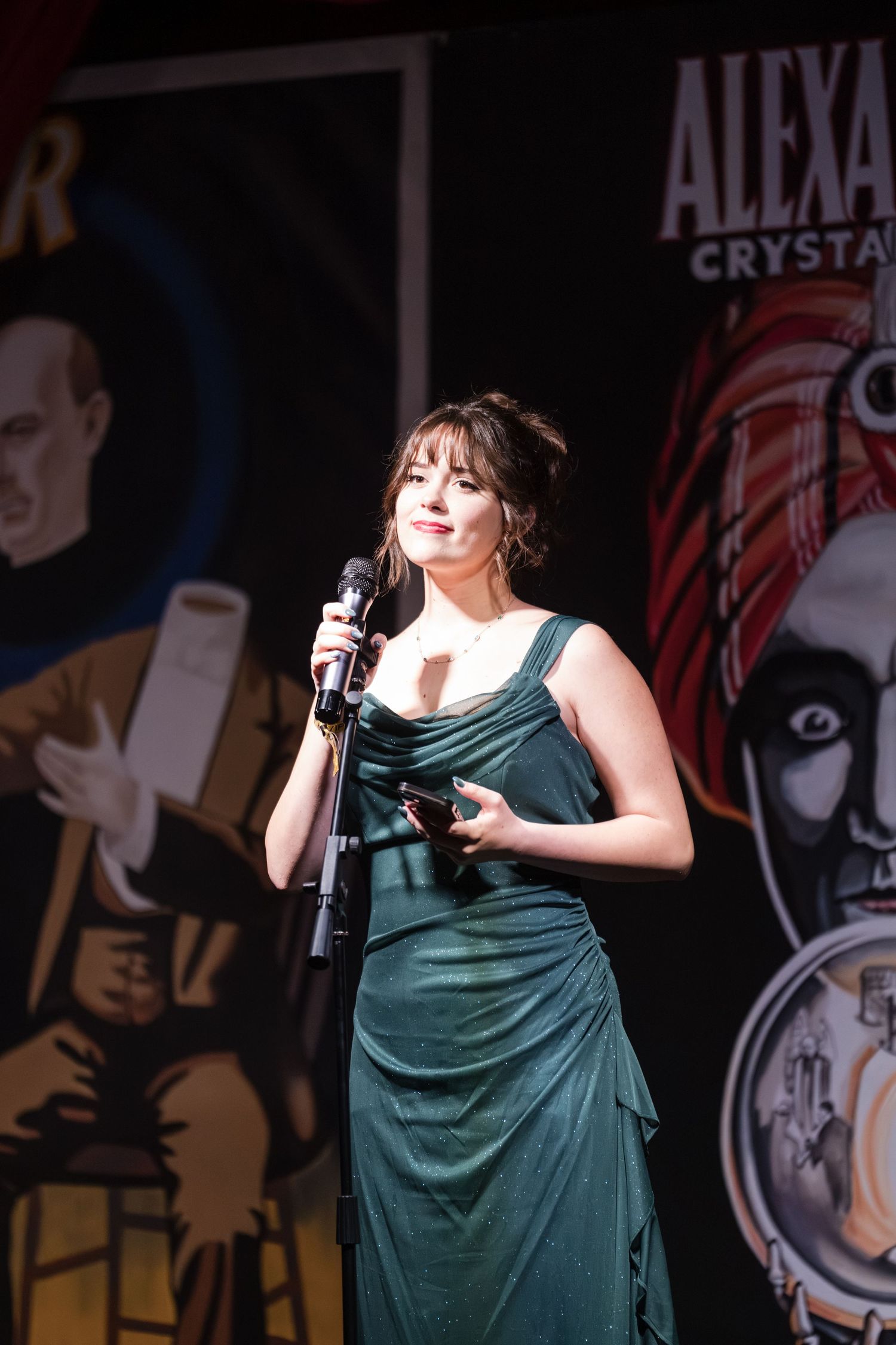 A performer in a green dress sings passionately on stage during a live performance.