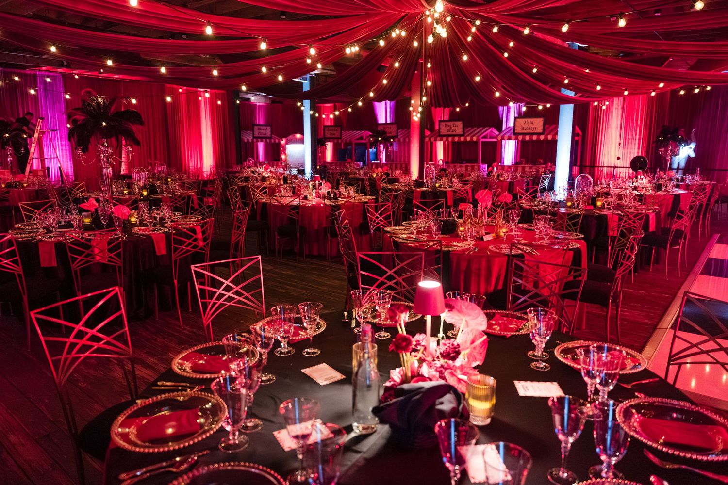 Elegant banquet hall decorated in dramatic red lighting with round tables and cross-back chairs set for a formal event.