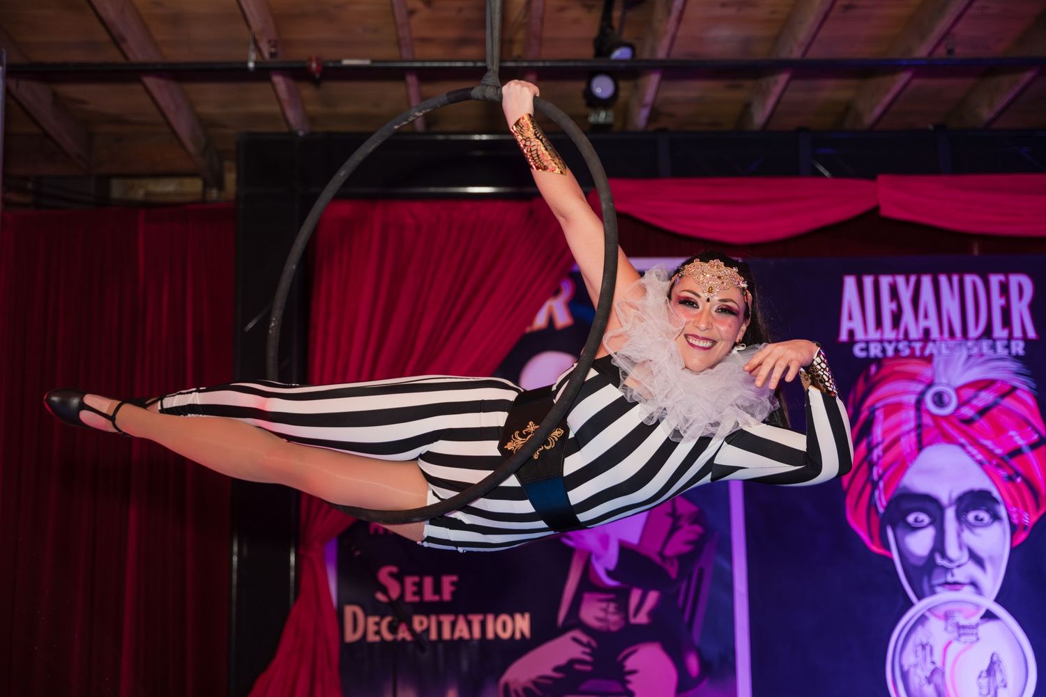 Performer in black and white striped outfit dances energetically on stage with red curtains and dramatic lighting.