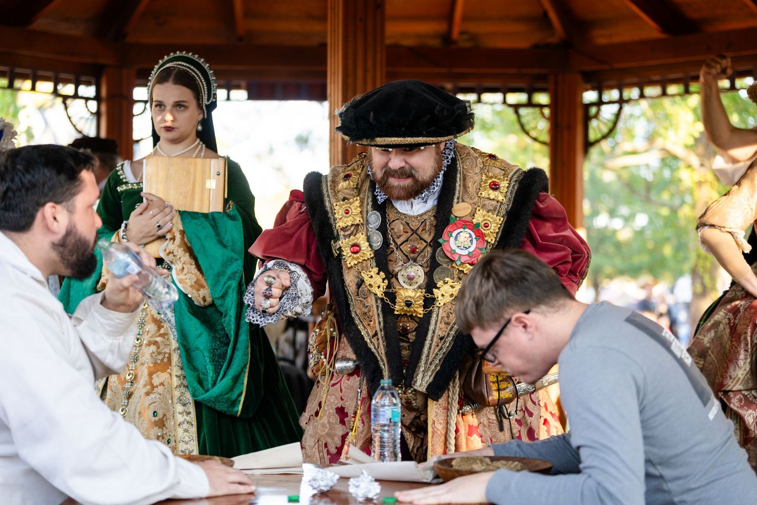People in medieval Renaissance costumes gather around a table during a historical reenactment event.