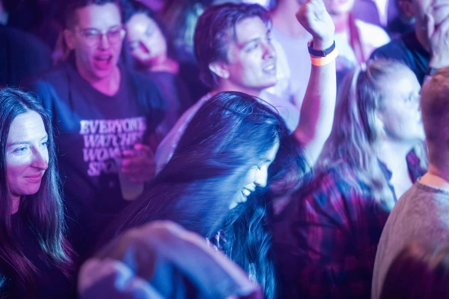 A crowd of people dancing and enjoying themselves at a nightclub with colorful purple lighting effects.