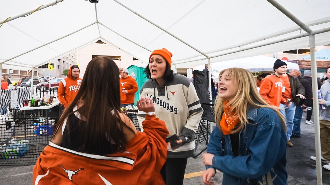Students in university gear socializing under a white tent at an outdoor gathering.