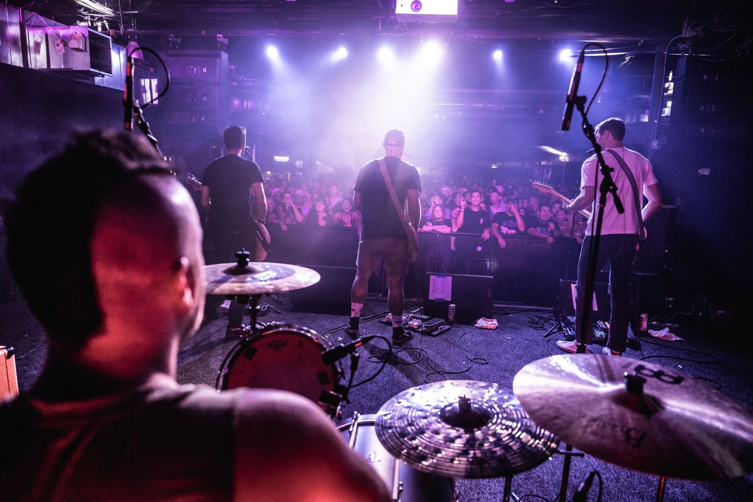 Band performs on stage with dramatic lighting while crowd watches in foreground.