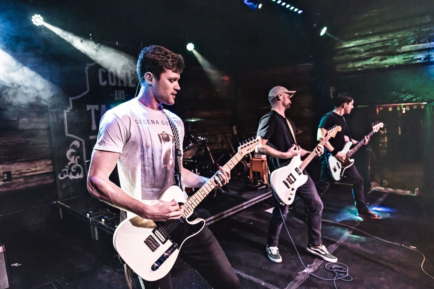 Musicians play electric guitars during performance with smoke and stage lighting effects.