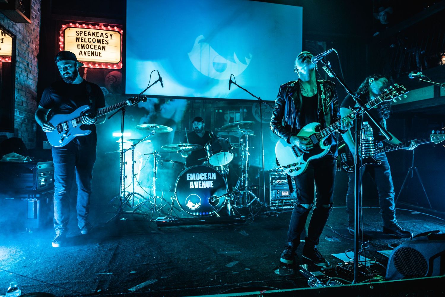 Full band performing on stage with drum kit and blue lighting effects.