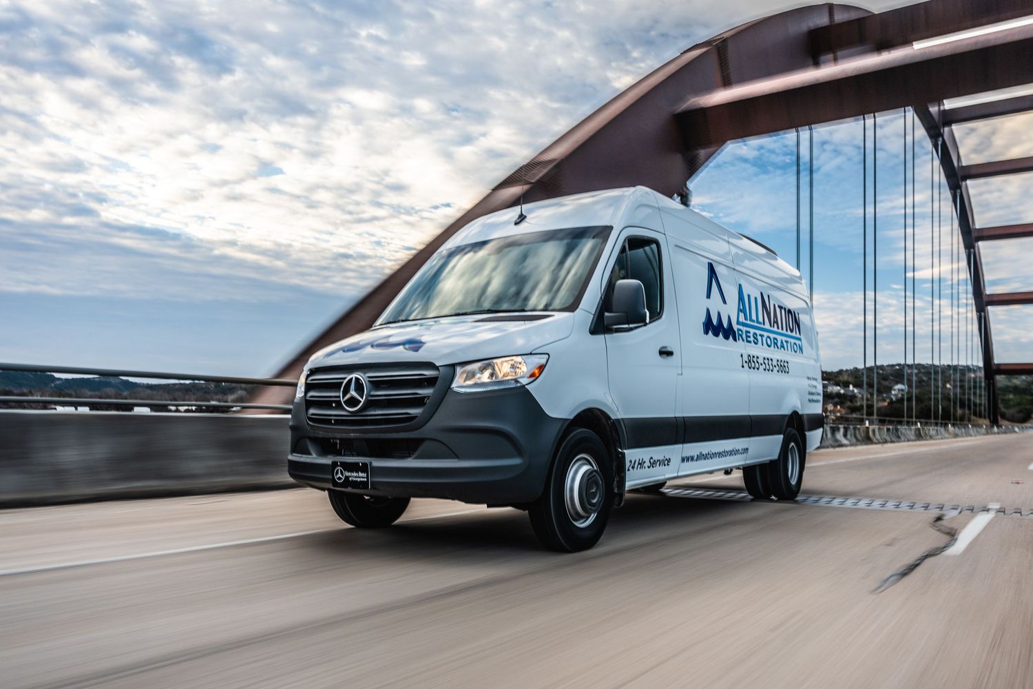Mercedes-Benz delivery van driving across bridge with cloudy sky backdrop.