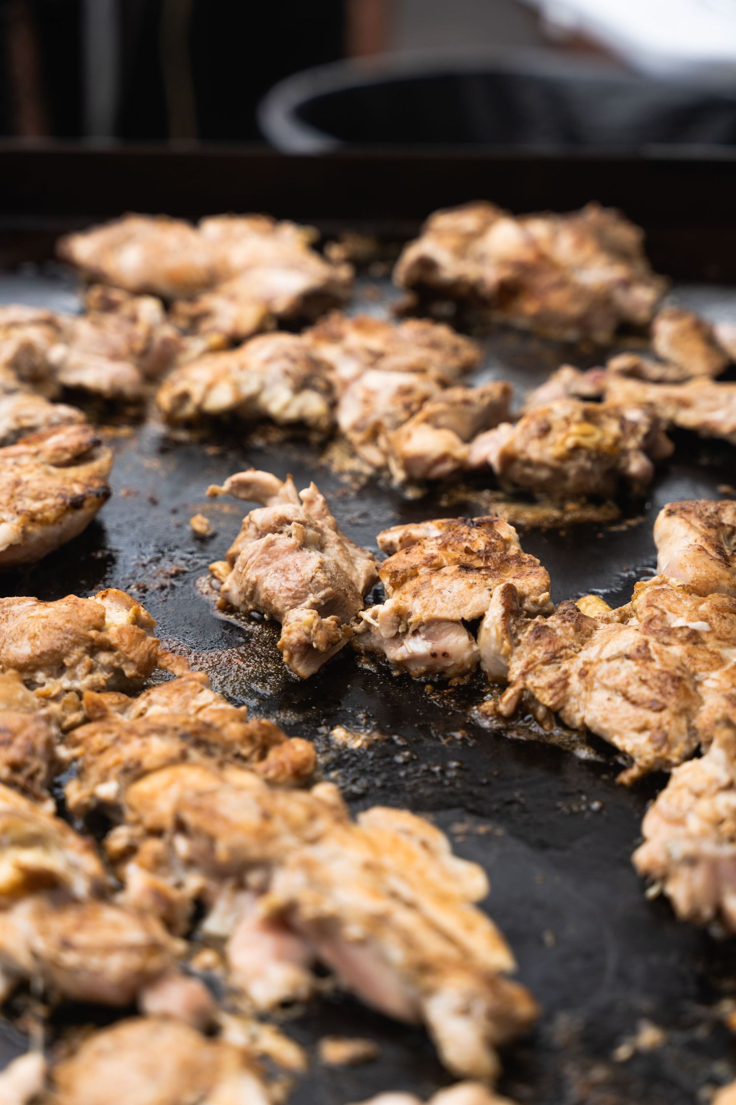 Grilled chicken pieces cooking on black griddle surface in close-up view.