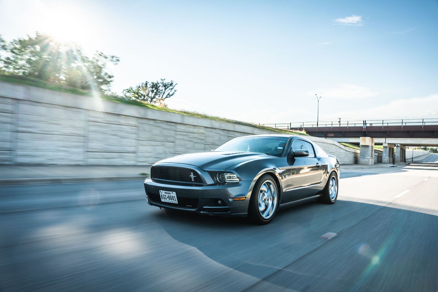 Modern Mustang sports car captured in dynamic rolling shot near highway.
